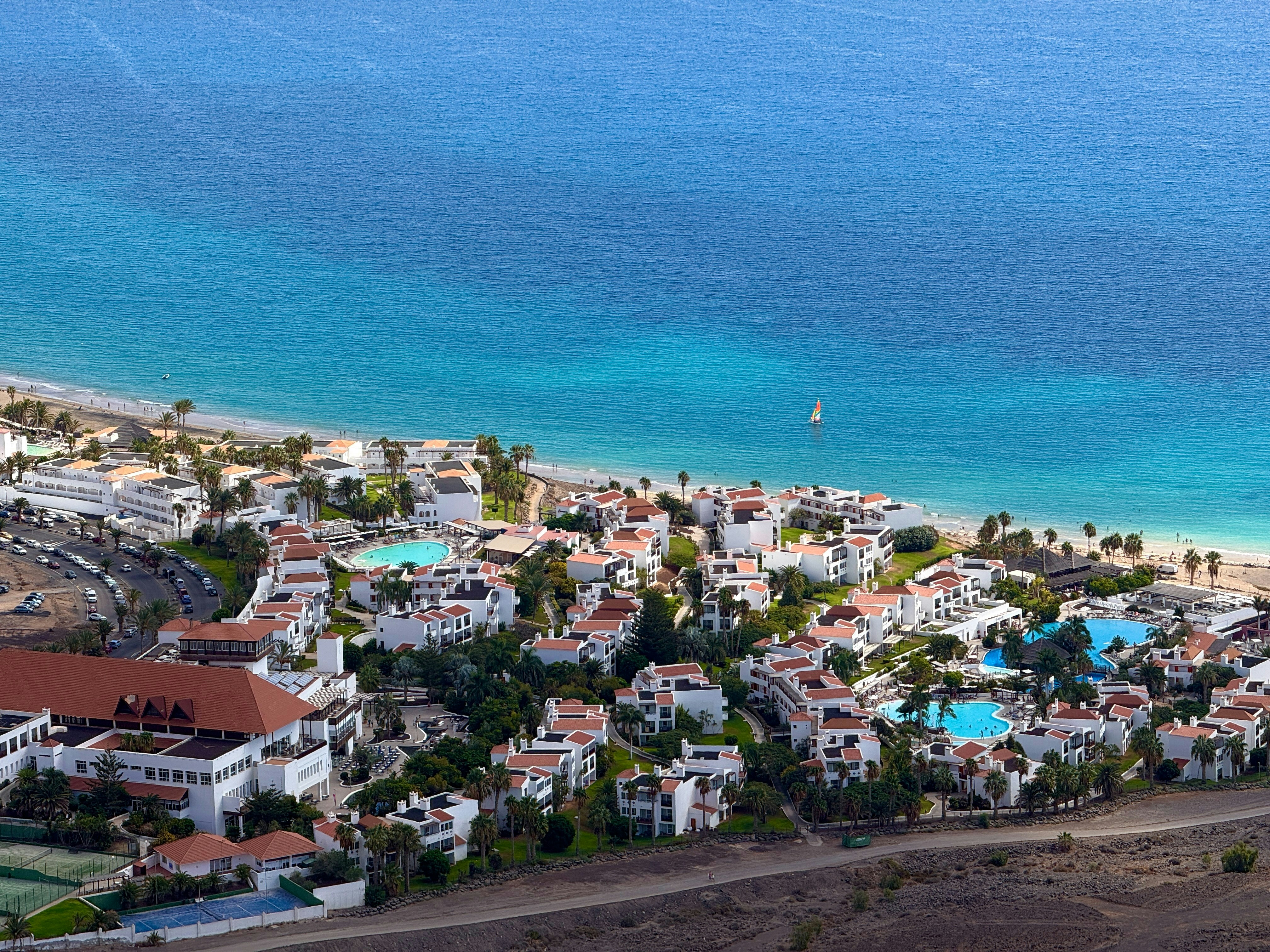 Aerial view of a white resort complex with swimming pools beside a blue ocean