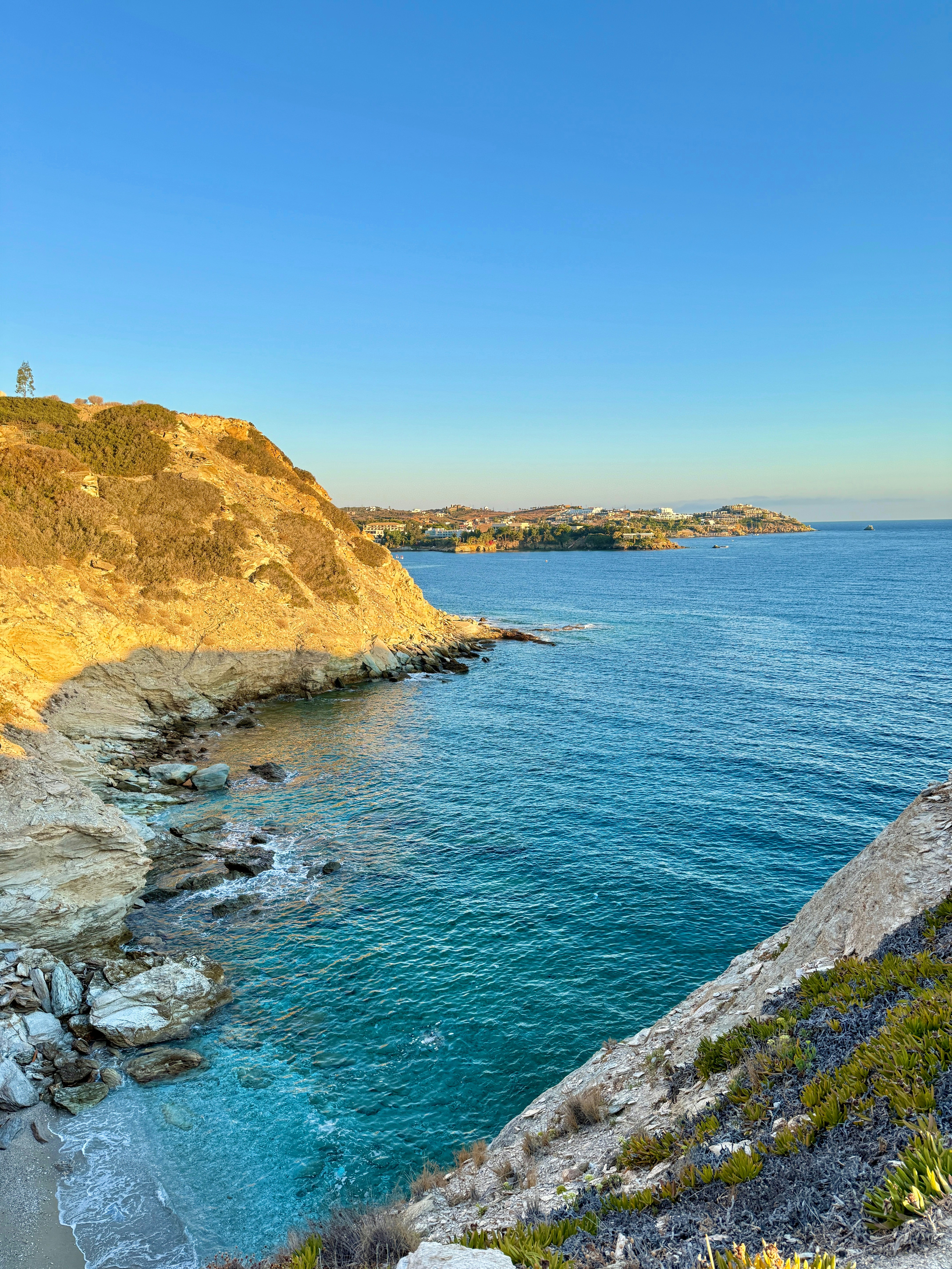A rocky cliffside overlooking a blue sea under a clear sky