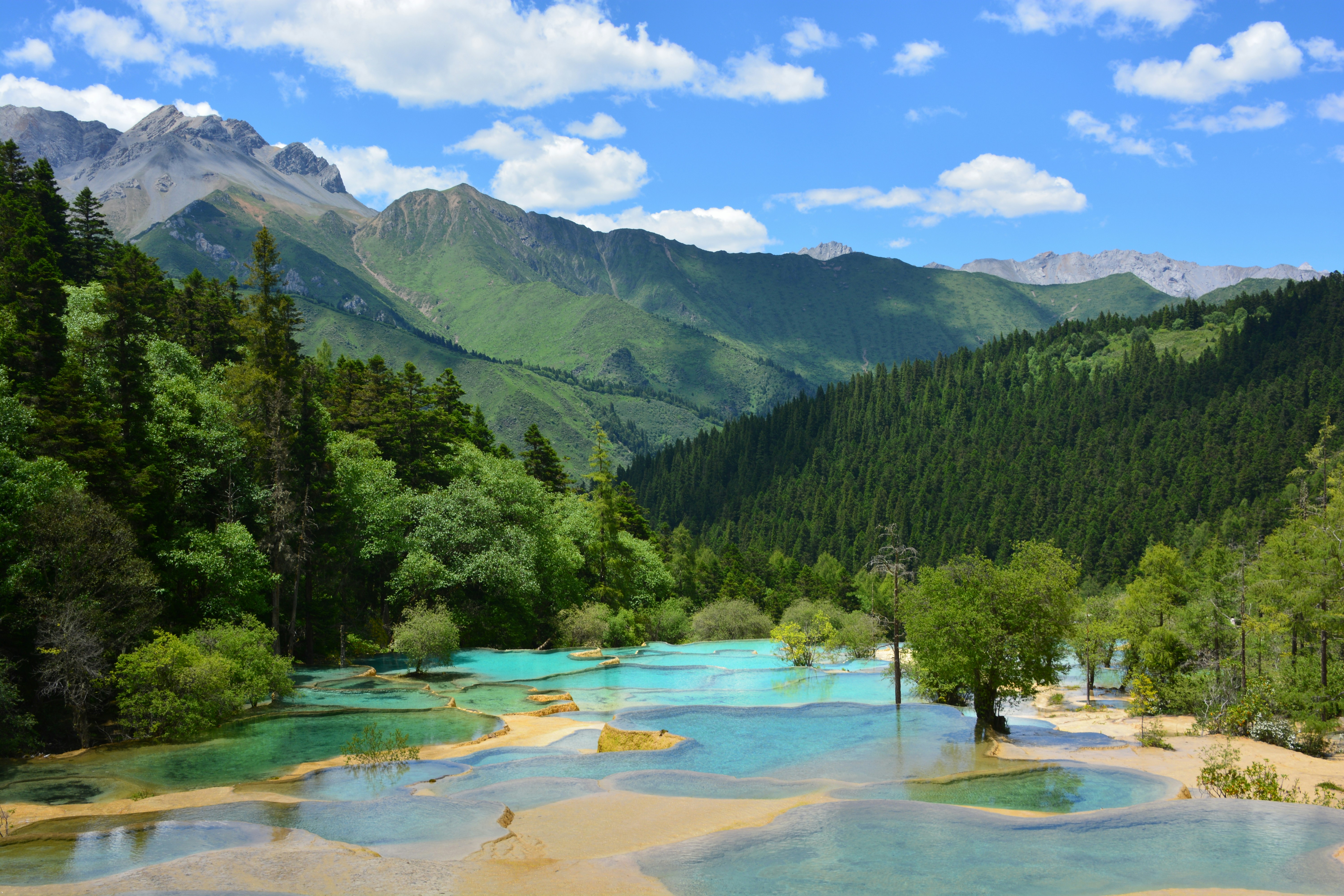 Turquoise pools in Huanglong National Park surrounded by green forests and mountain peaks