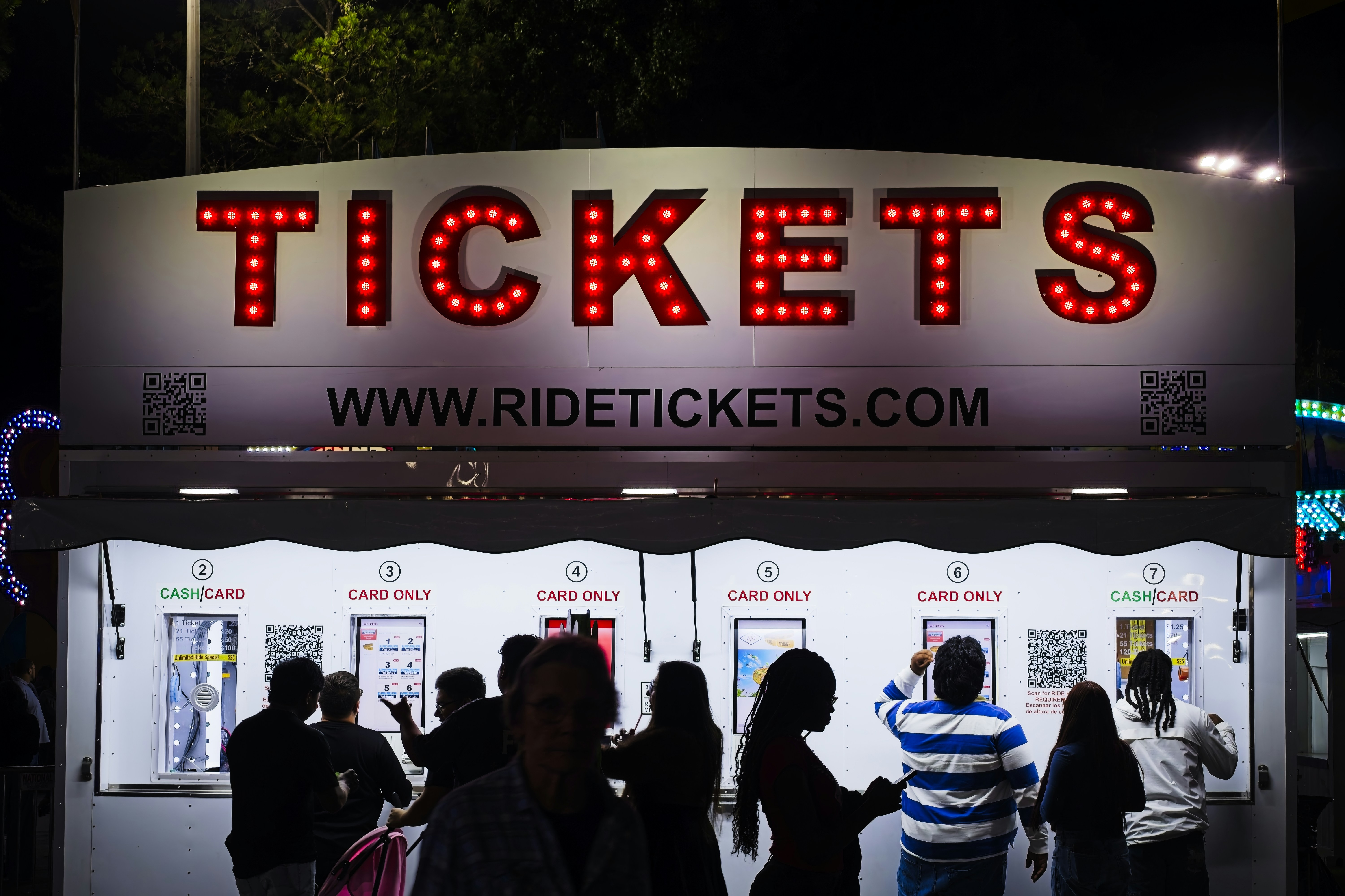People using automated kiosks at a ticket booth with a red illuminated sign