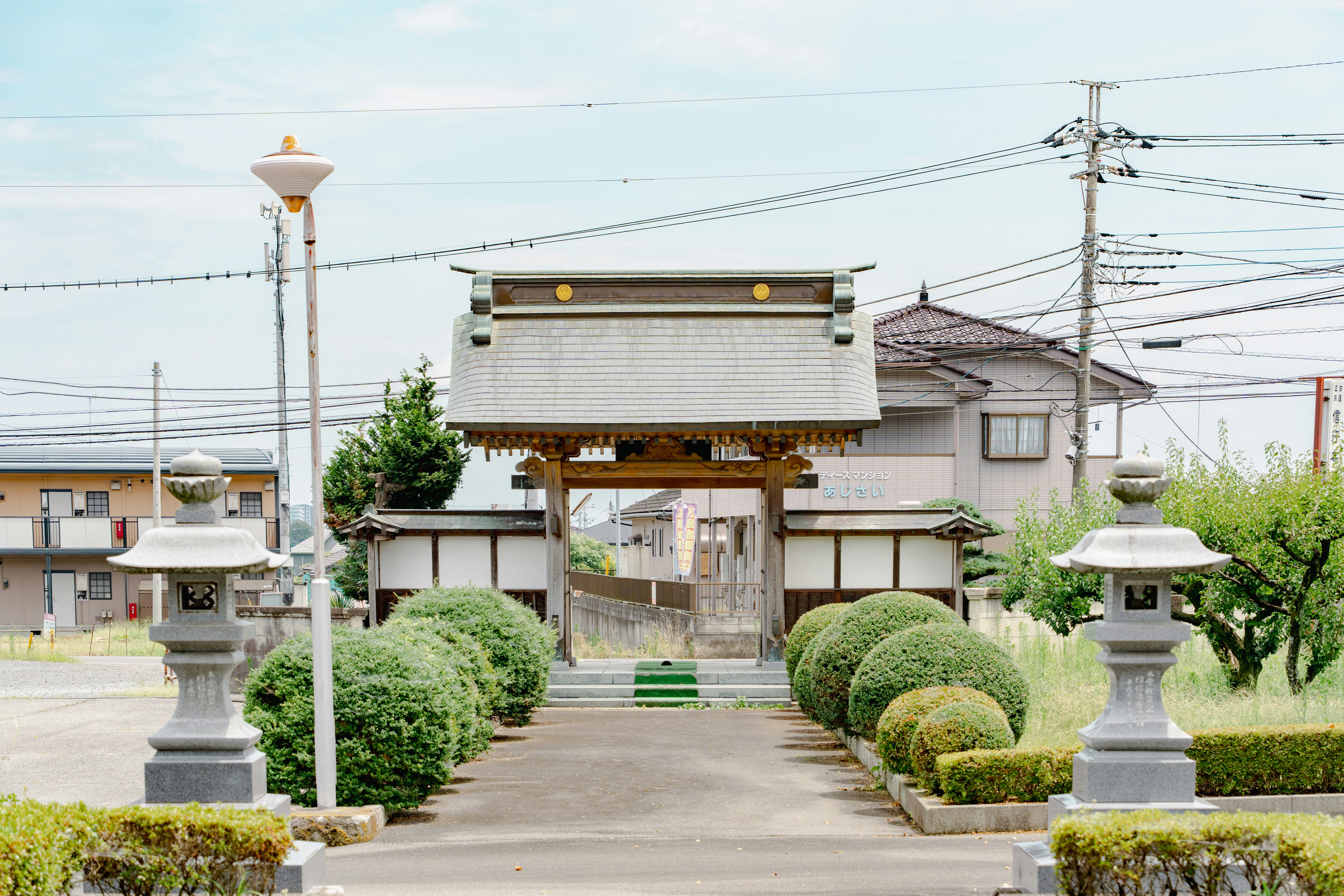 A traditional wooden gate with stone lanterns in a Japanese residential neighborhood