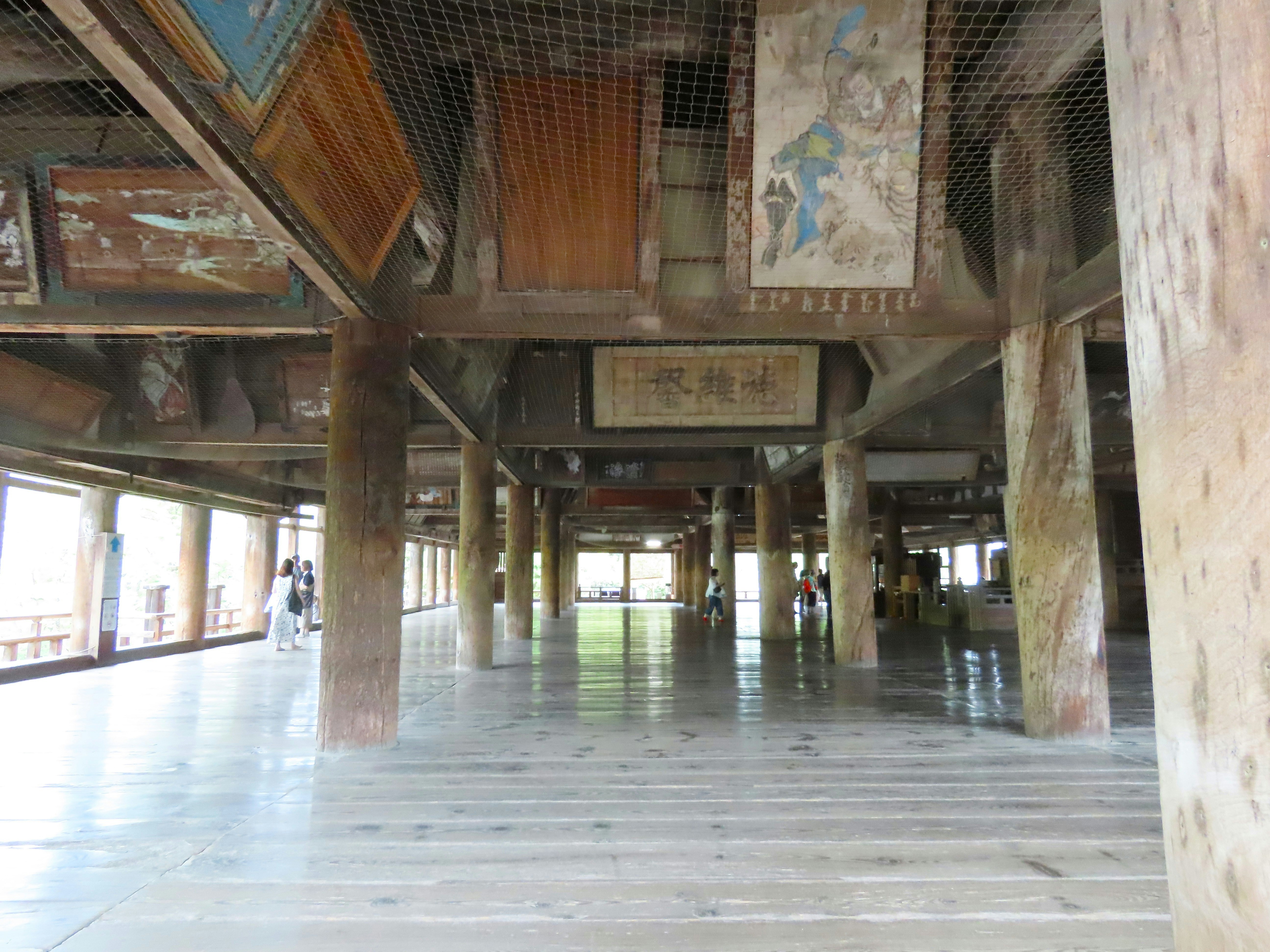 People walking on the wooden floor of a temple hall with large pillars