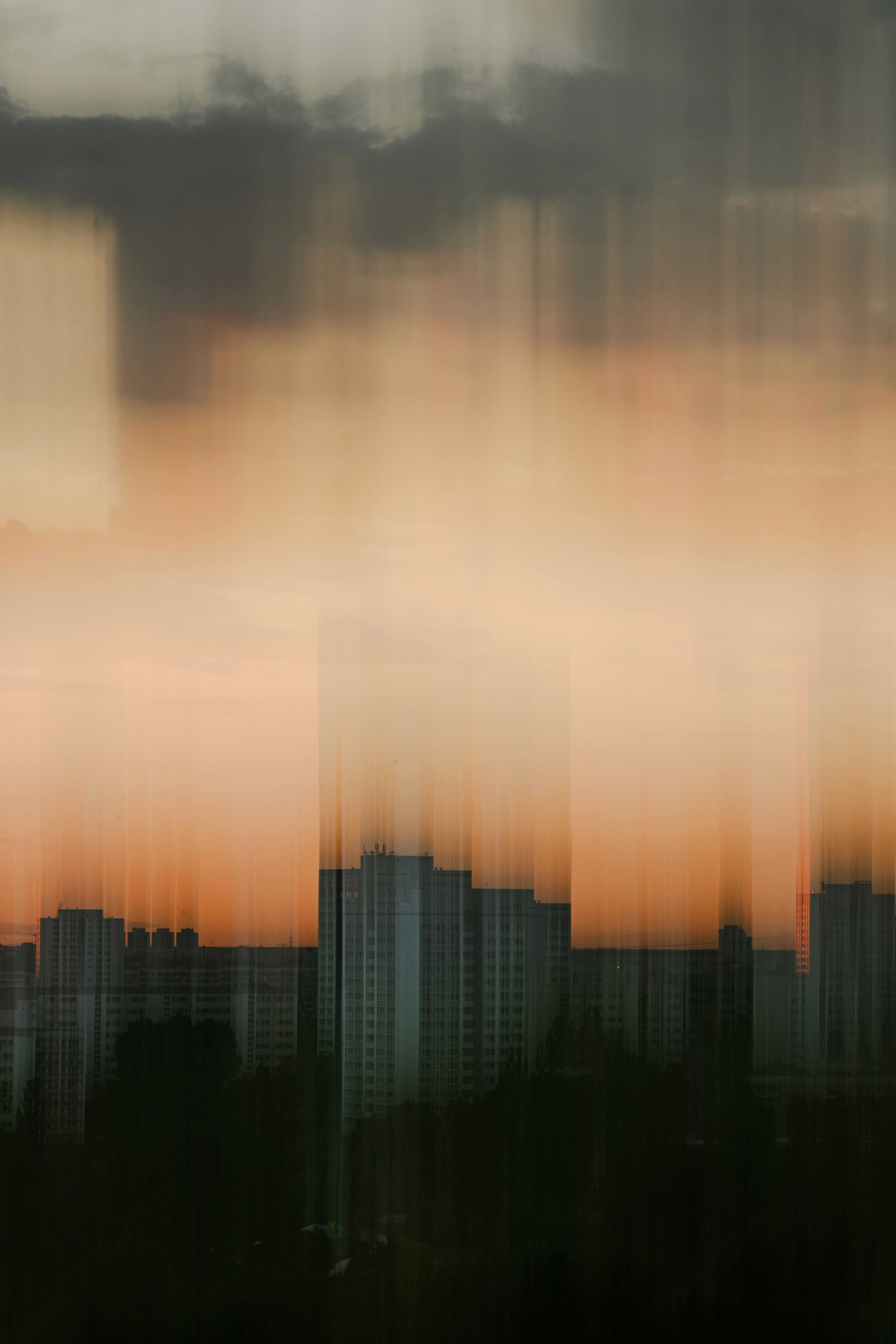 Tall apartment buildings silhouetted against a warm orange sky with vertical motion blur