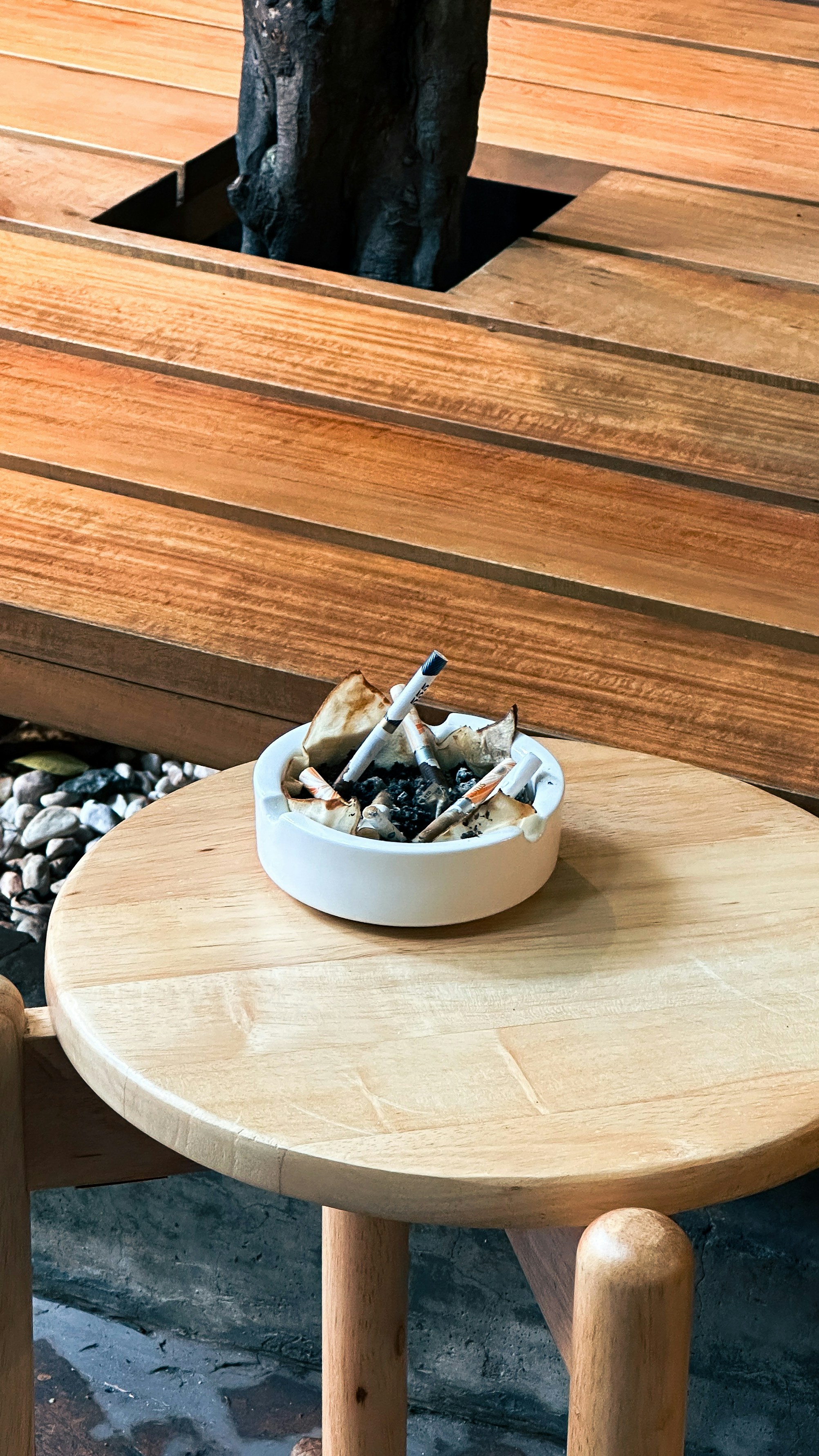 A white ceramic ashtray with cigarette butts on a round wooden table