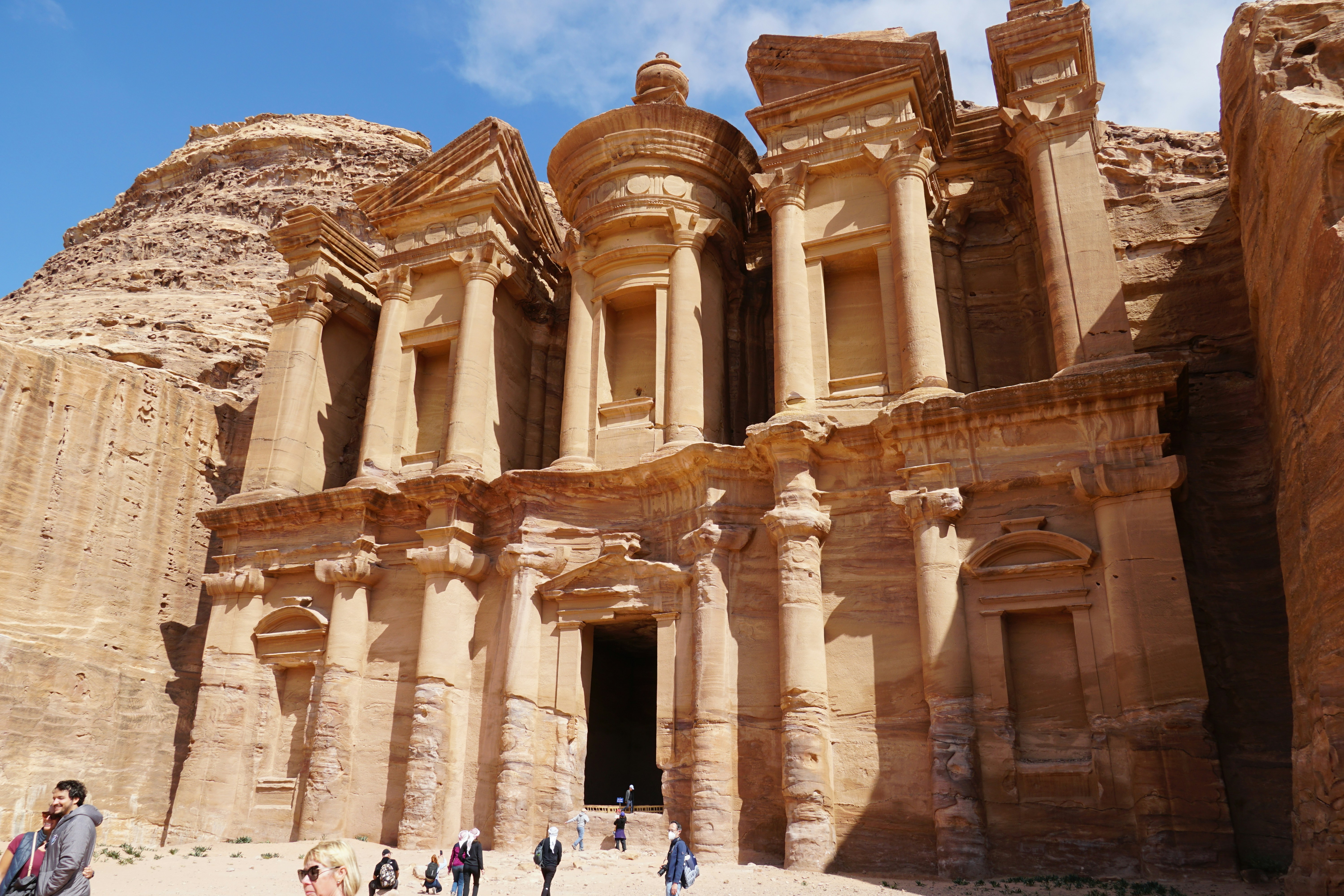 O Mosteiro esculpido em penhascos de arenito em Petra, Jordânia, com pessoas caminhando por baixo
