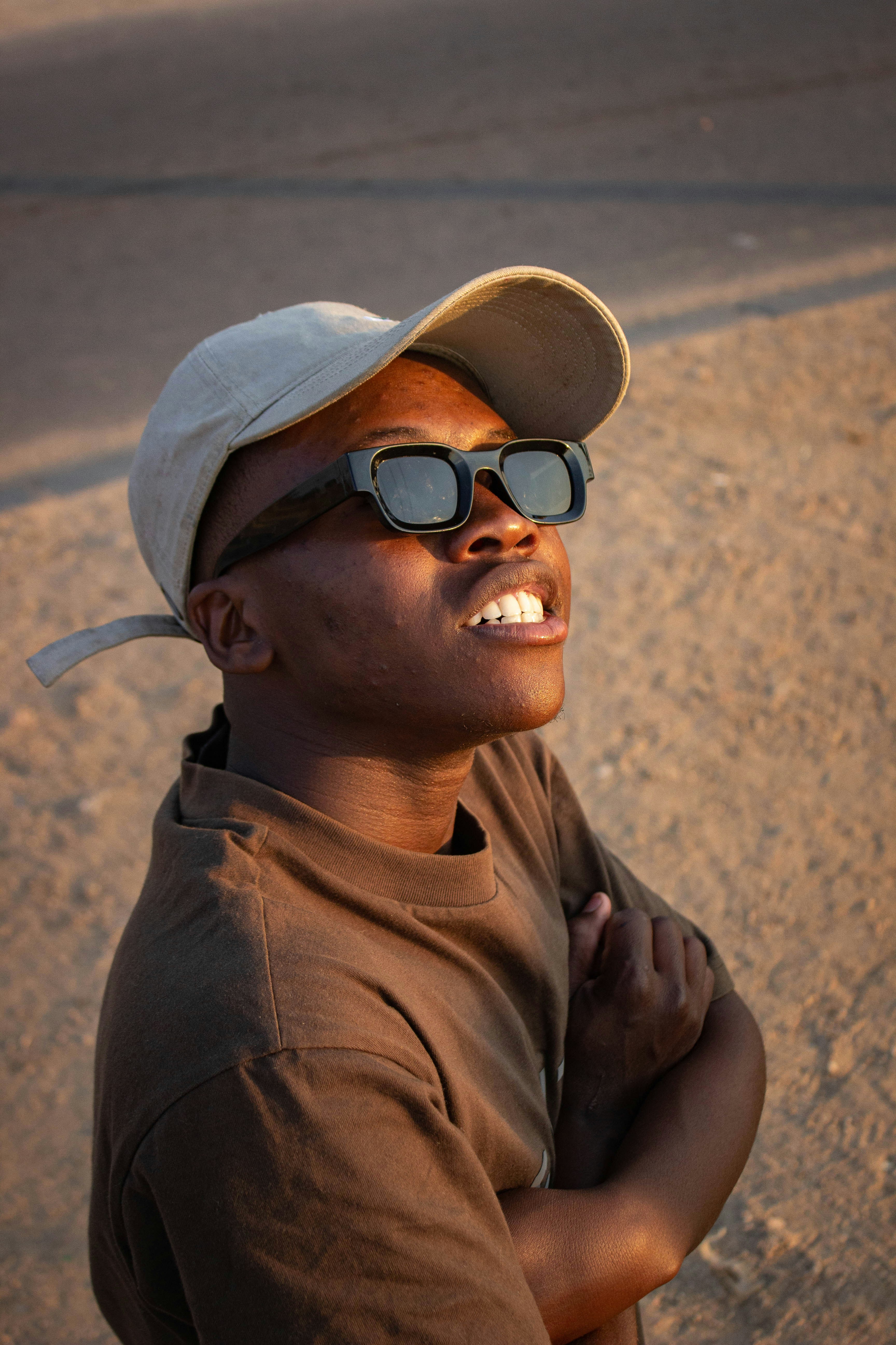 A person in a beige cap and sunglasses looking up in golden hour light