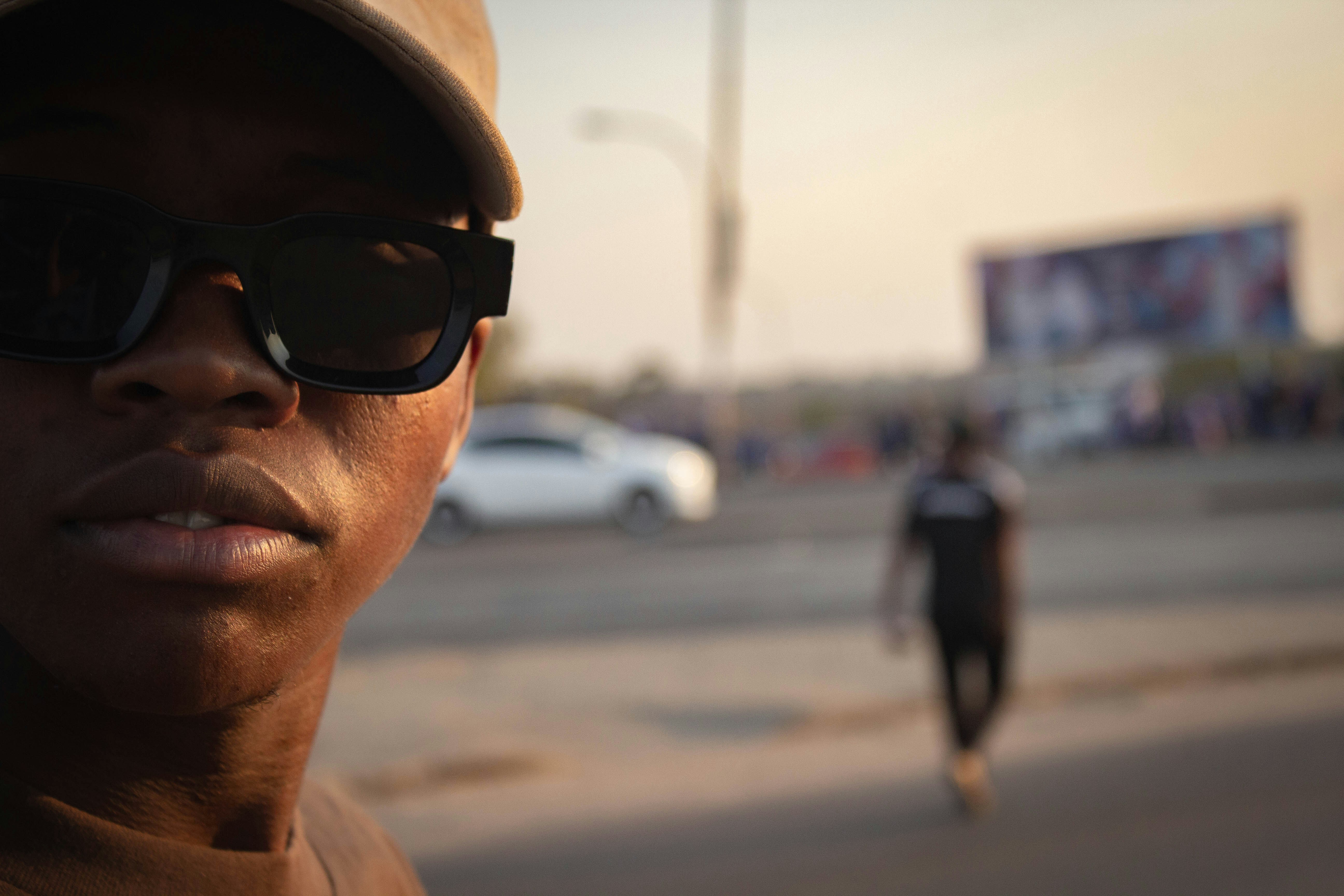 A person in sunglasses and a cap against a blurred urban street background