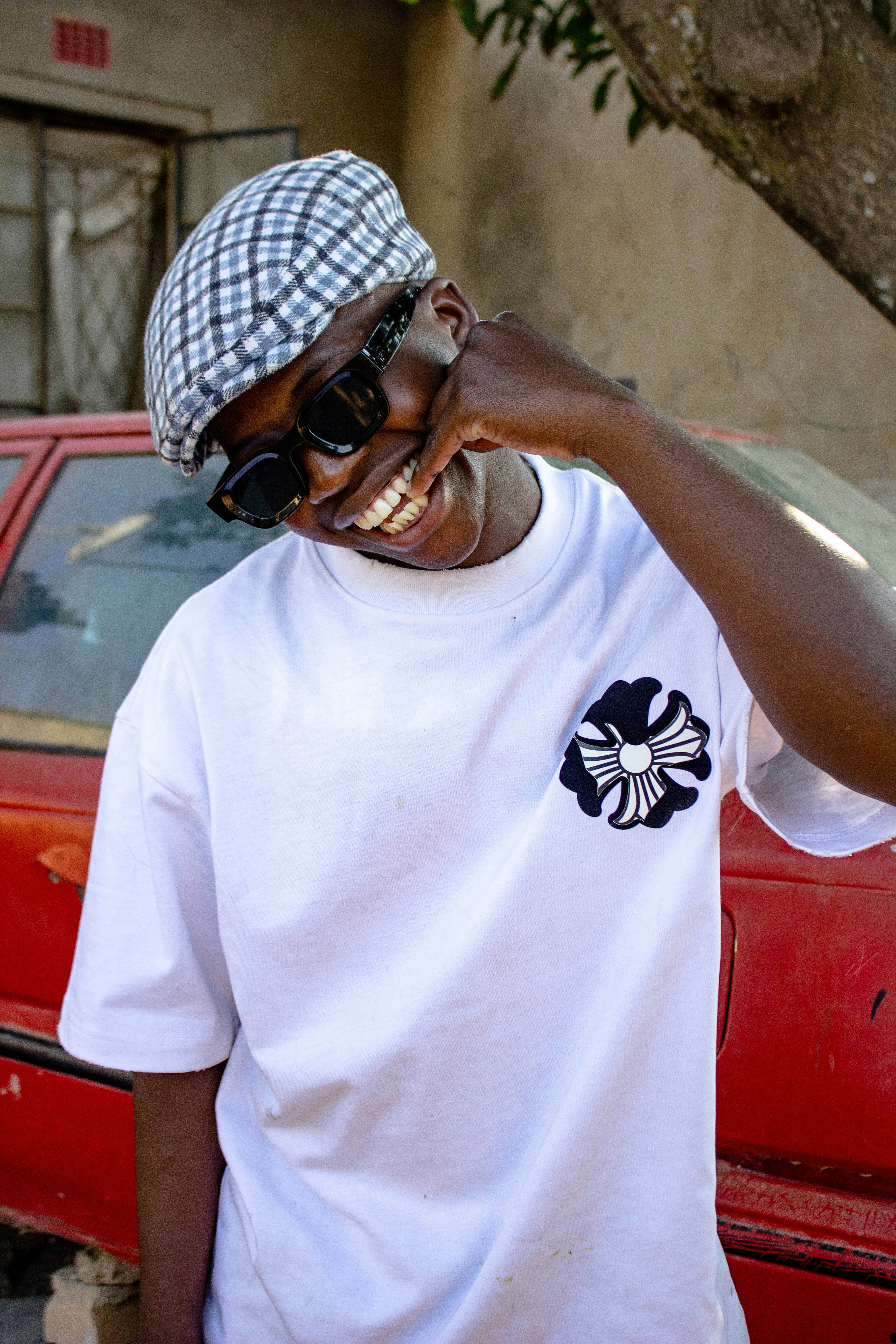 A smiling person in a plaid cap and white t-shirt before a red car