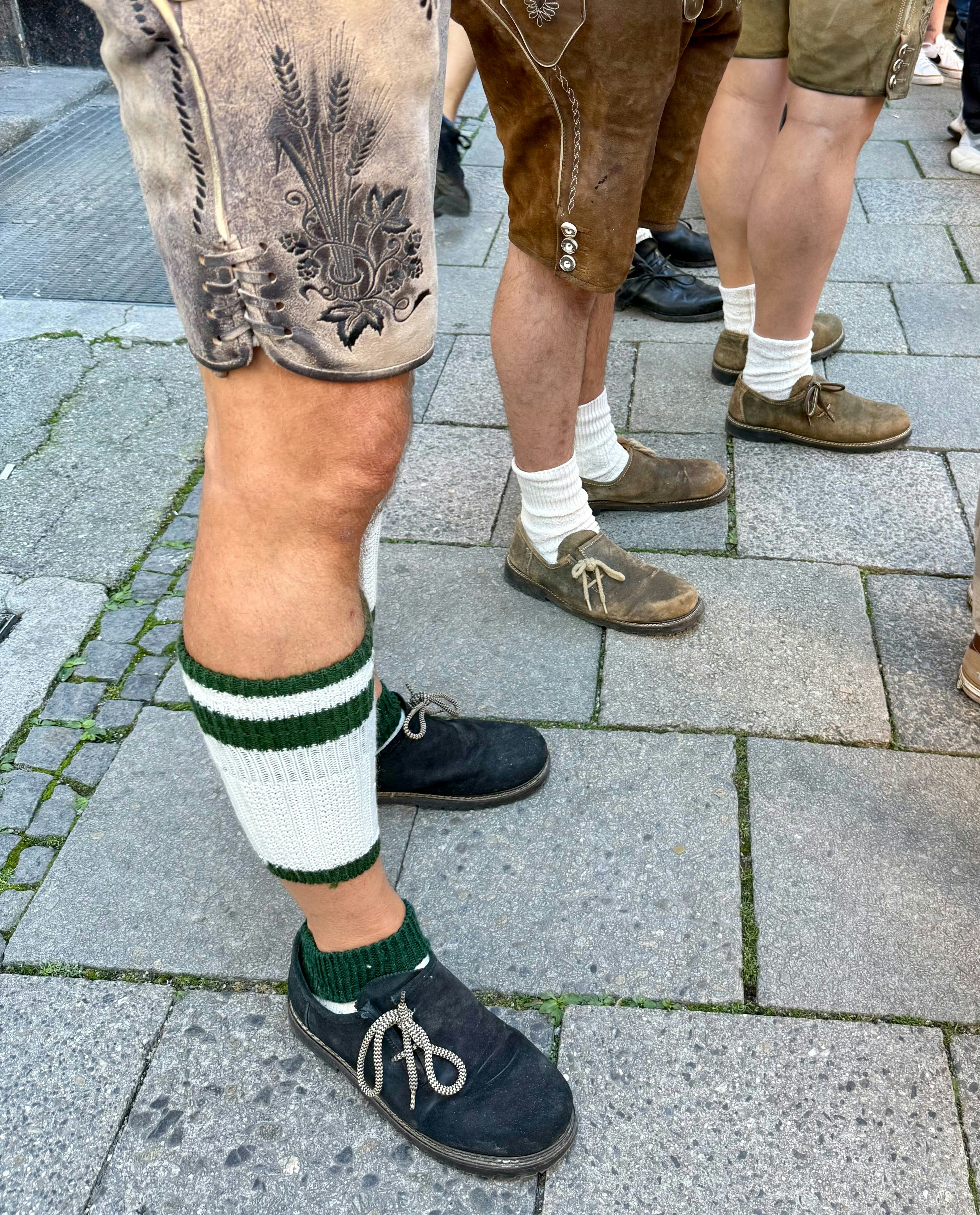 People wearing traditional leather lederhosen and socks on a stone paved street