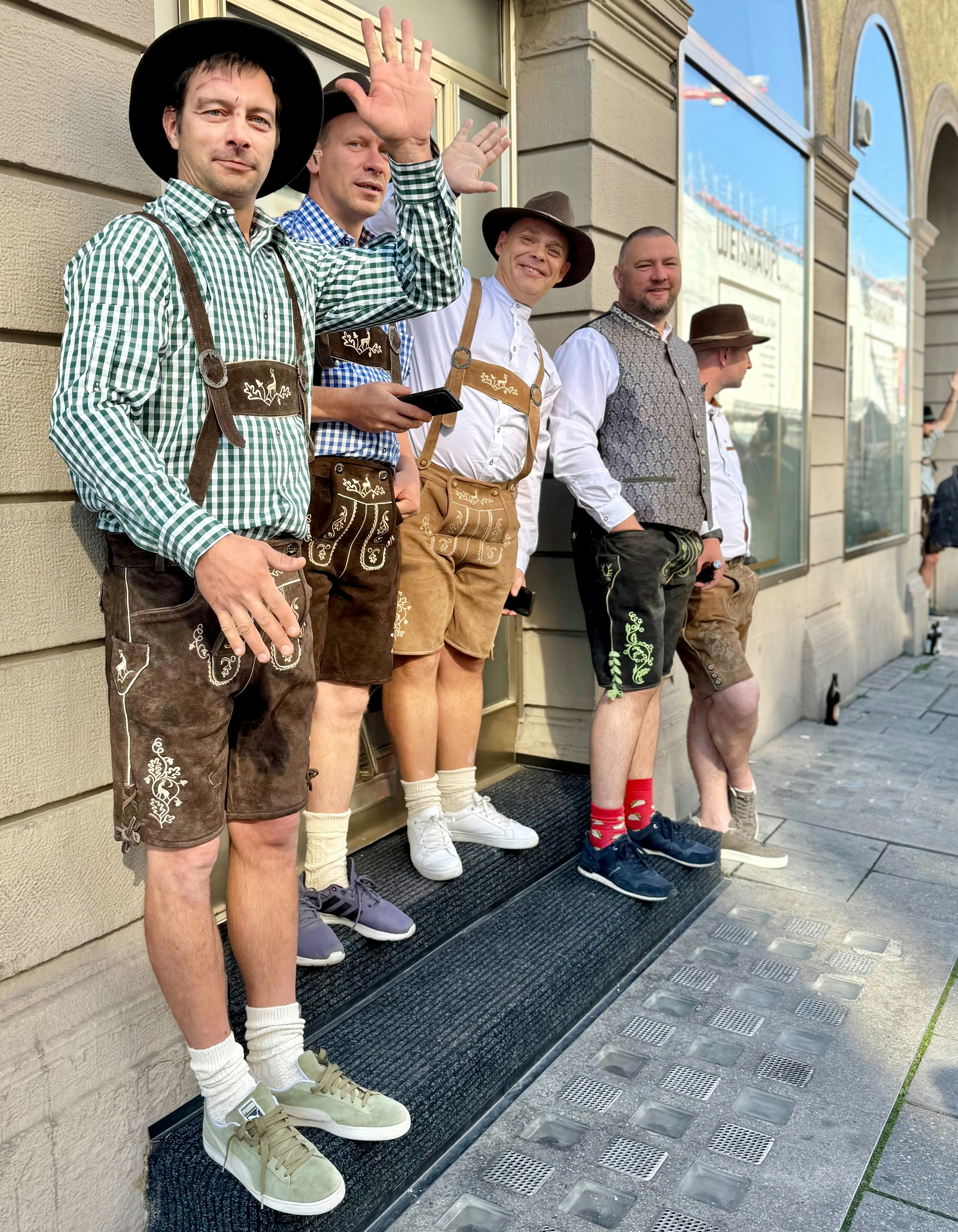 Five men in traditional Bavarian lederhosen and hats standing outside a building
