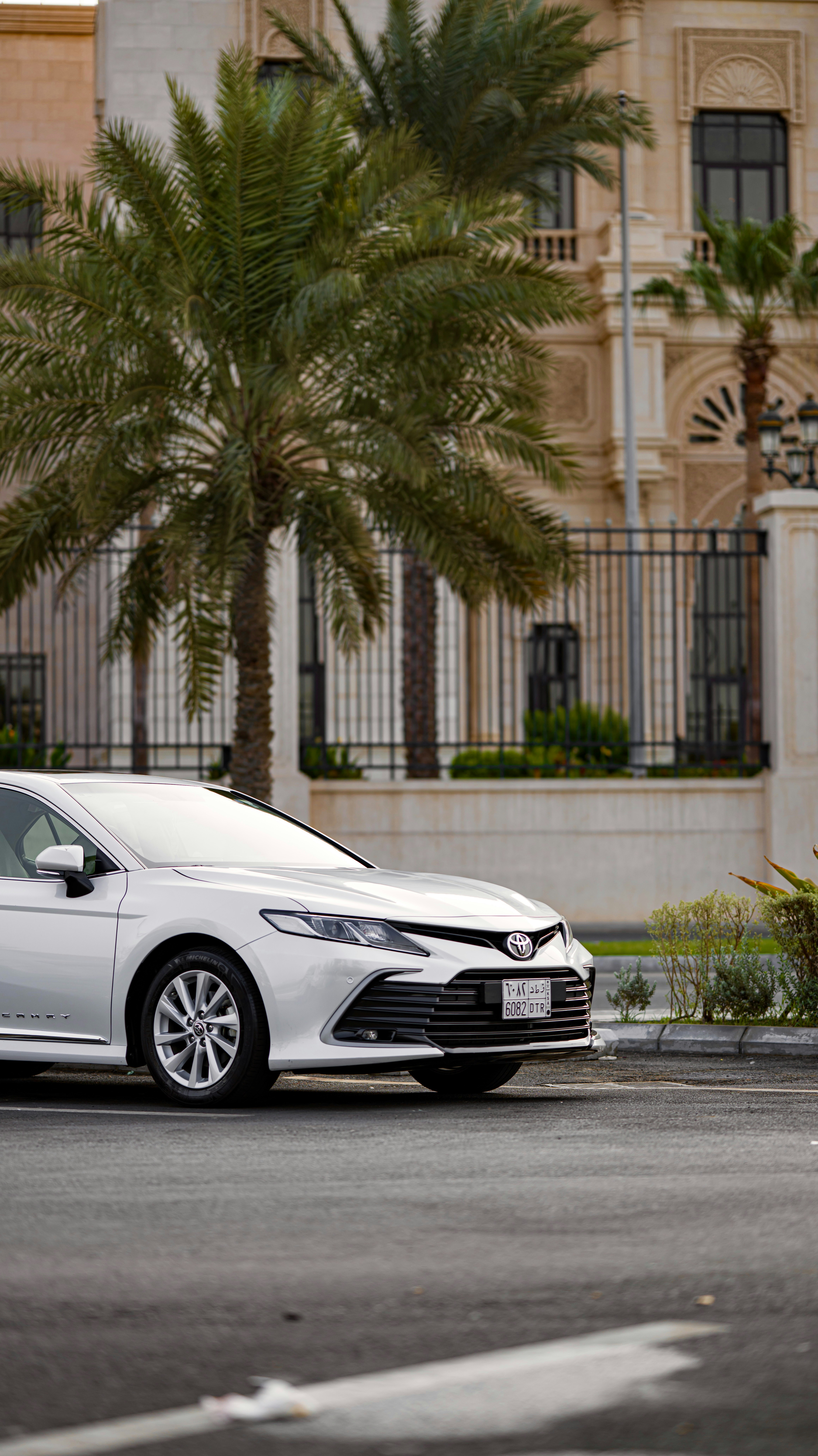 A white Toyota Camry parked on a street near a palm tree and building