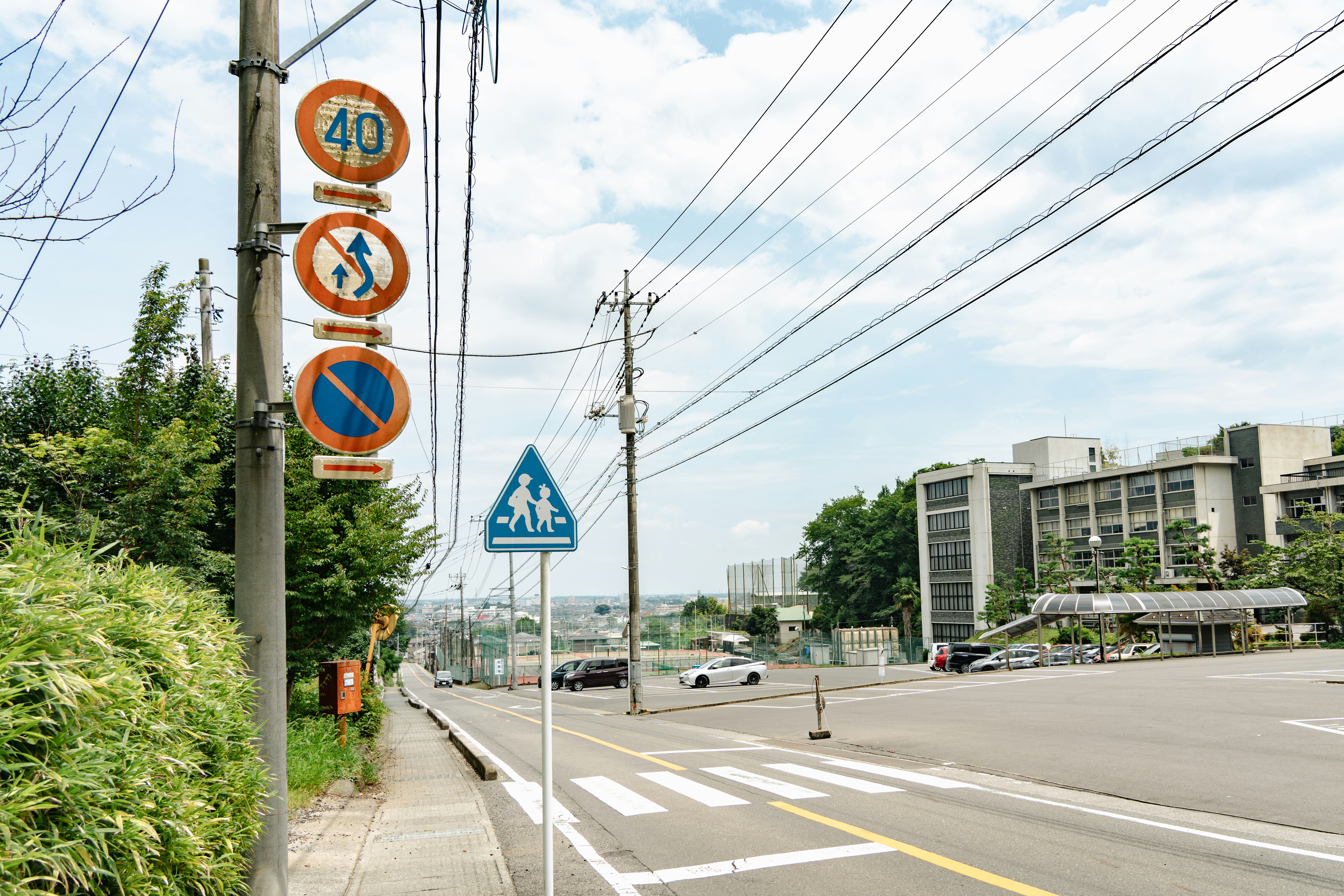 Japanese traffic signs on a pole beside a crosswalk and a parking lot