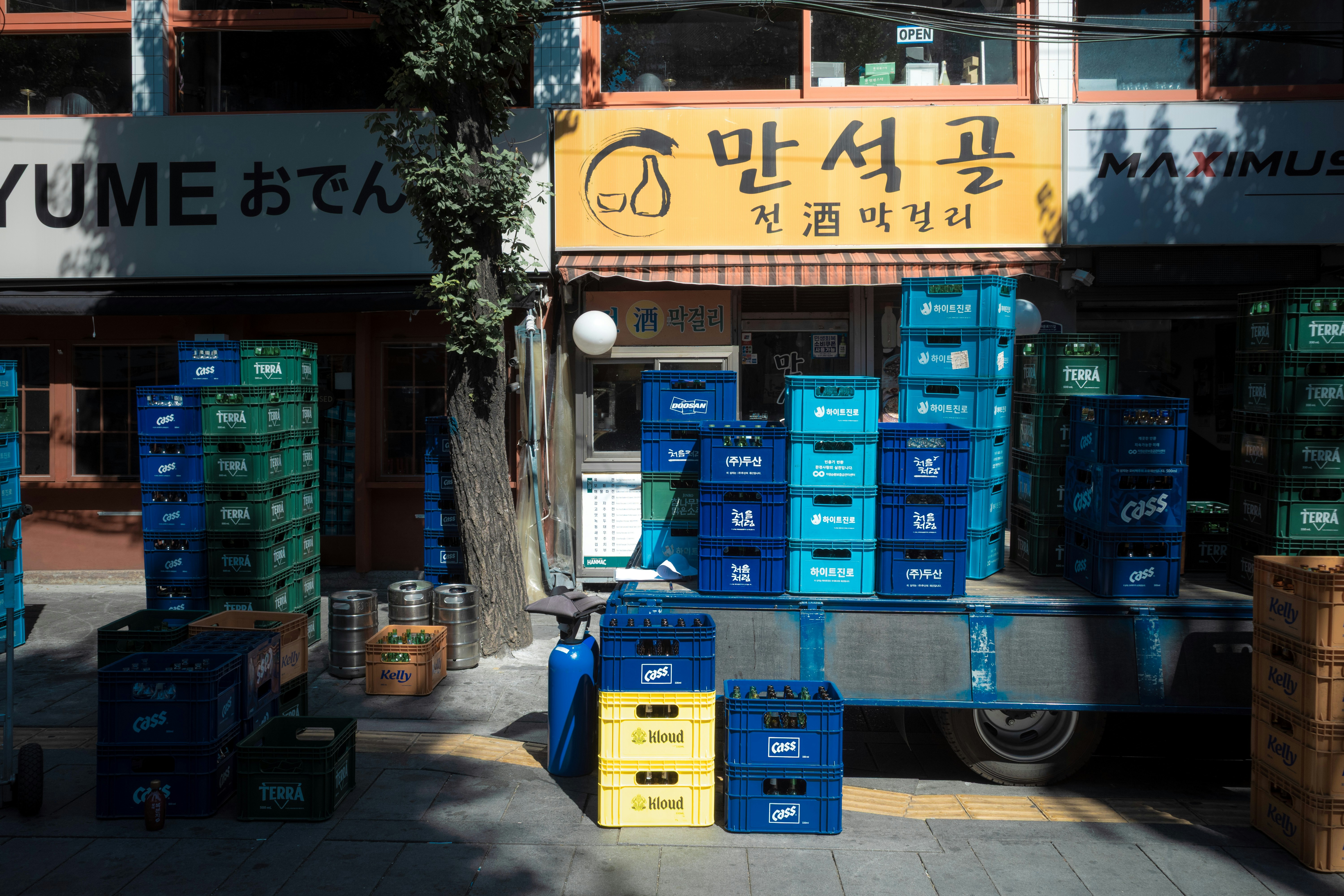 Stacks of colorful plastic beverage crates on a truck and sidewalk outside a restaurant