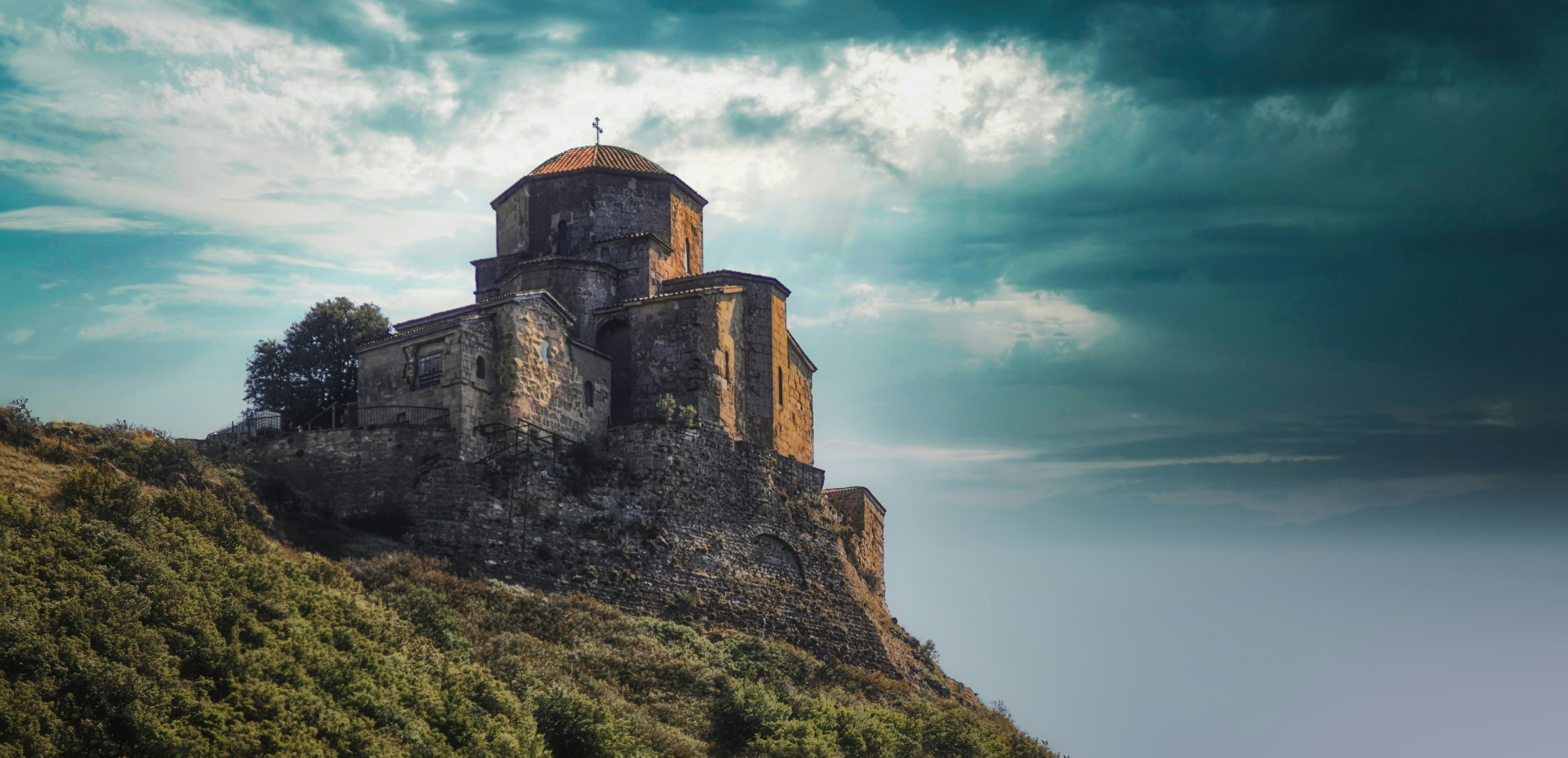 An ancient stone church on a grassy hill under a dramatic cloudy sky