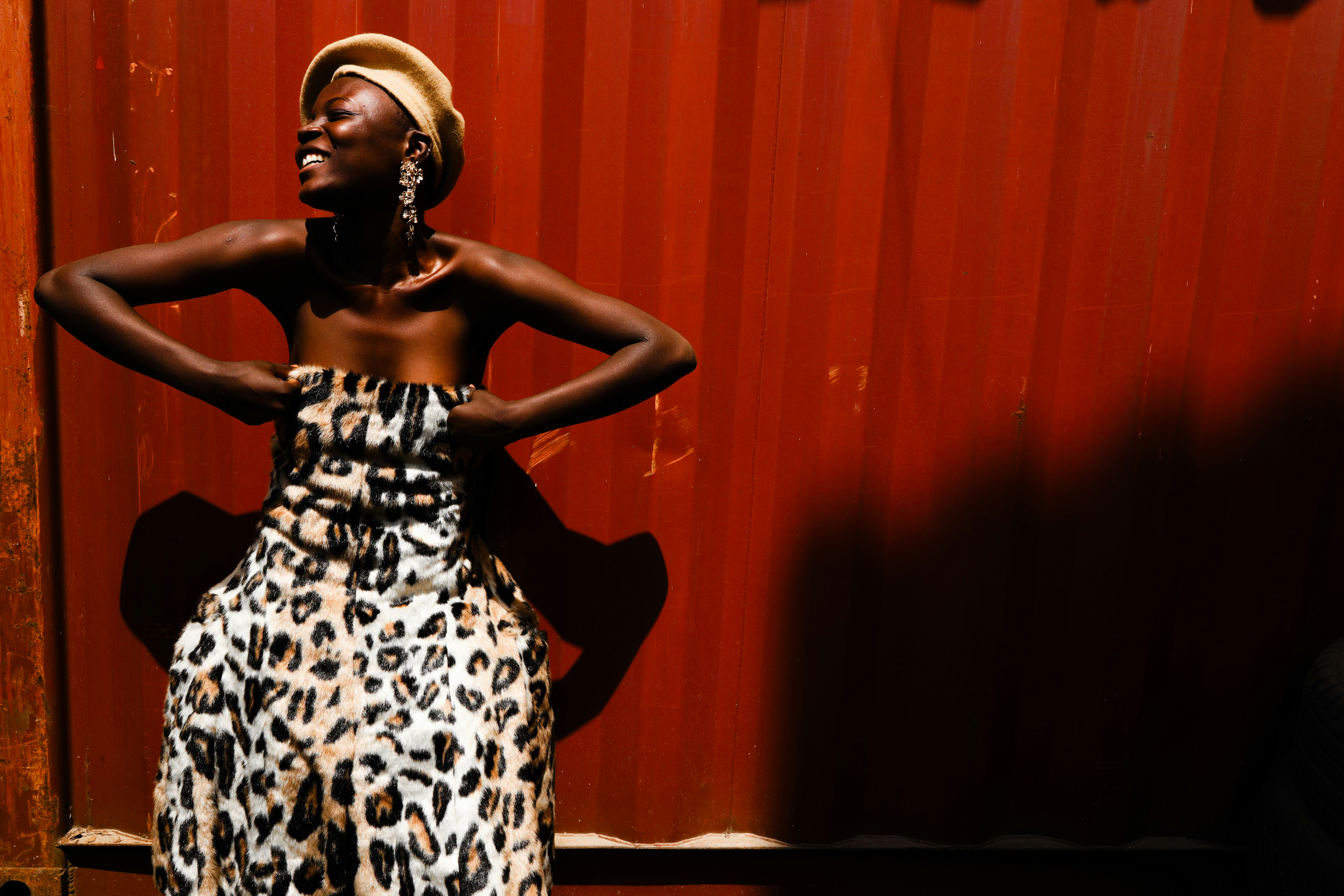 A woman in a leopard print dress and beret against a red corrugated wall
