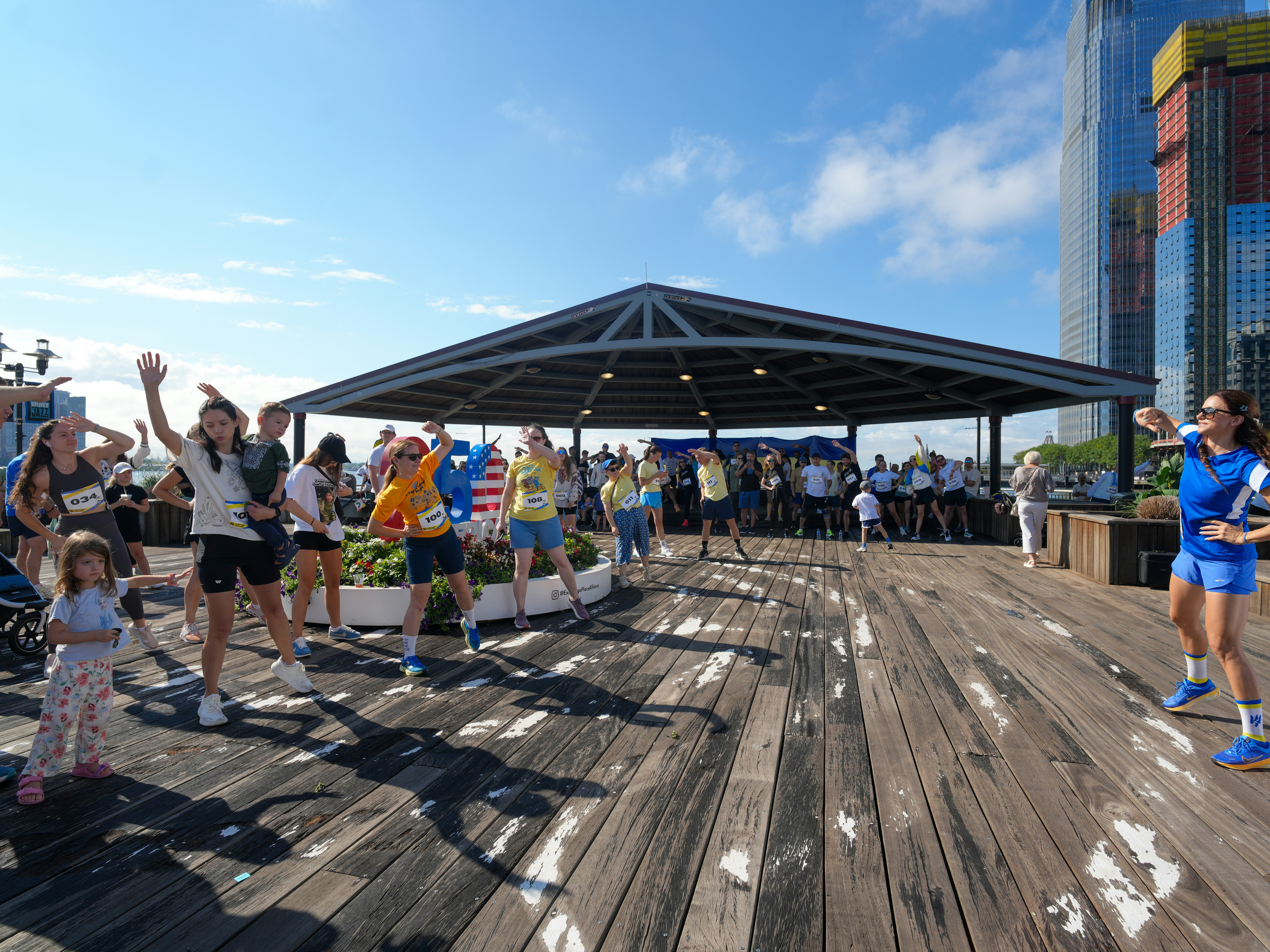 A group of people stretching on a wooden pier during a sunny outdoor workout