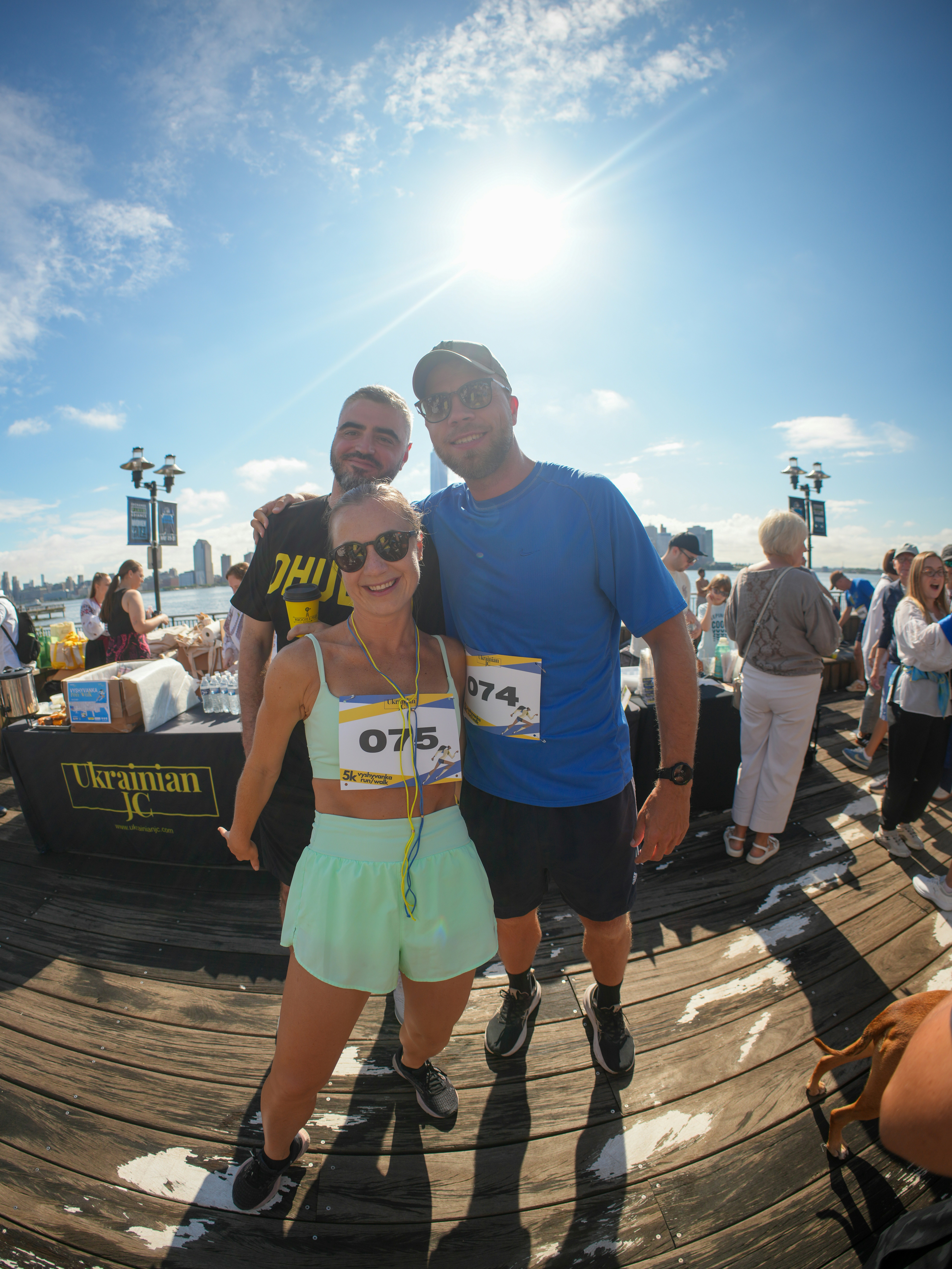 Three people in athletic gear posing on a wooden pier under bright sunlight