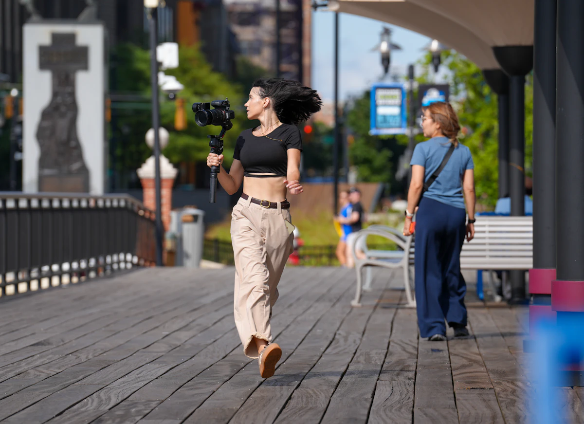 A vlogger walks along a boardwalk filming with a camera on a gimbal