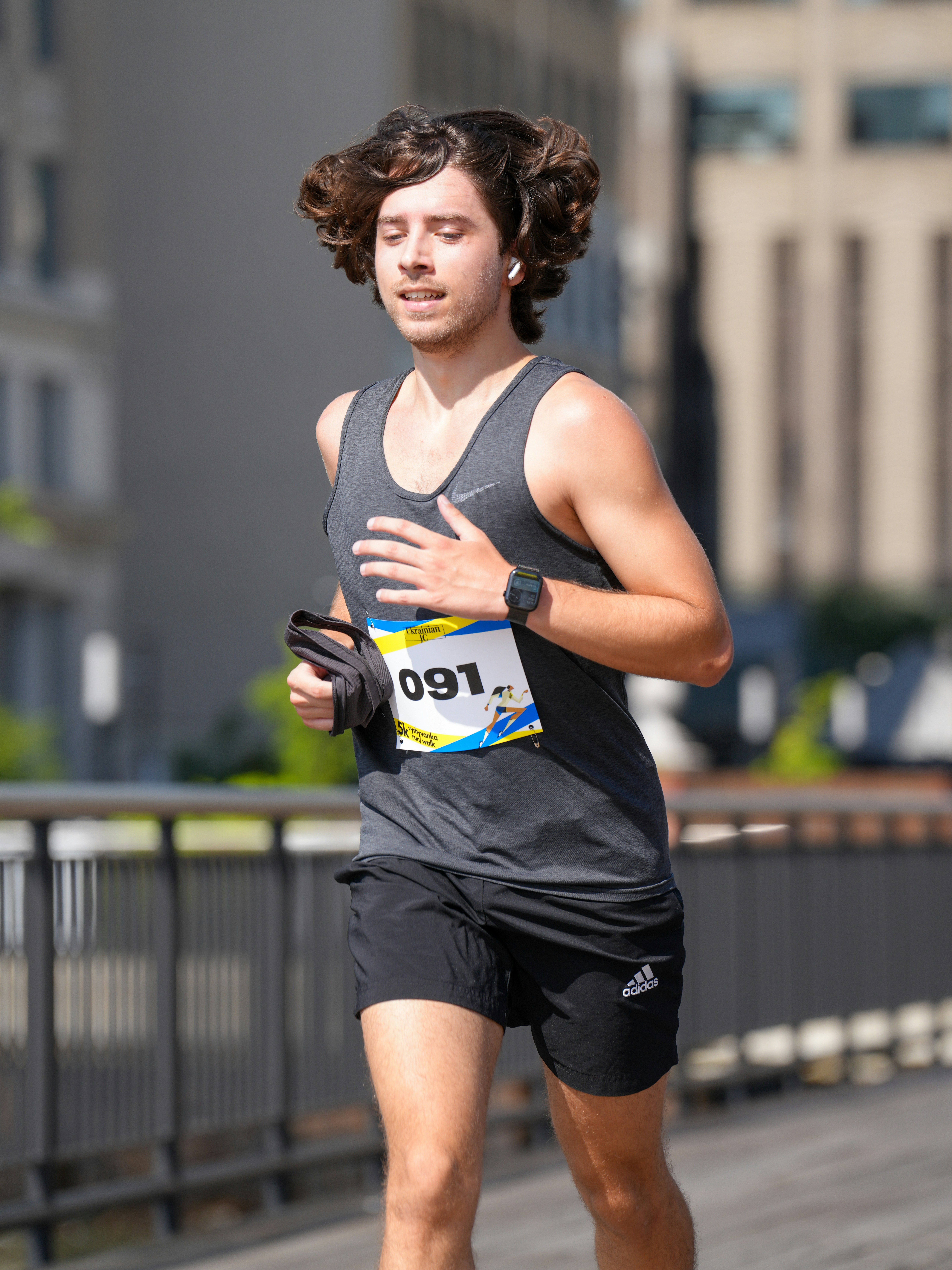 A man with long wavy hair running in a race wearing a bib