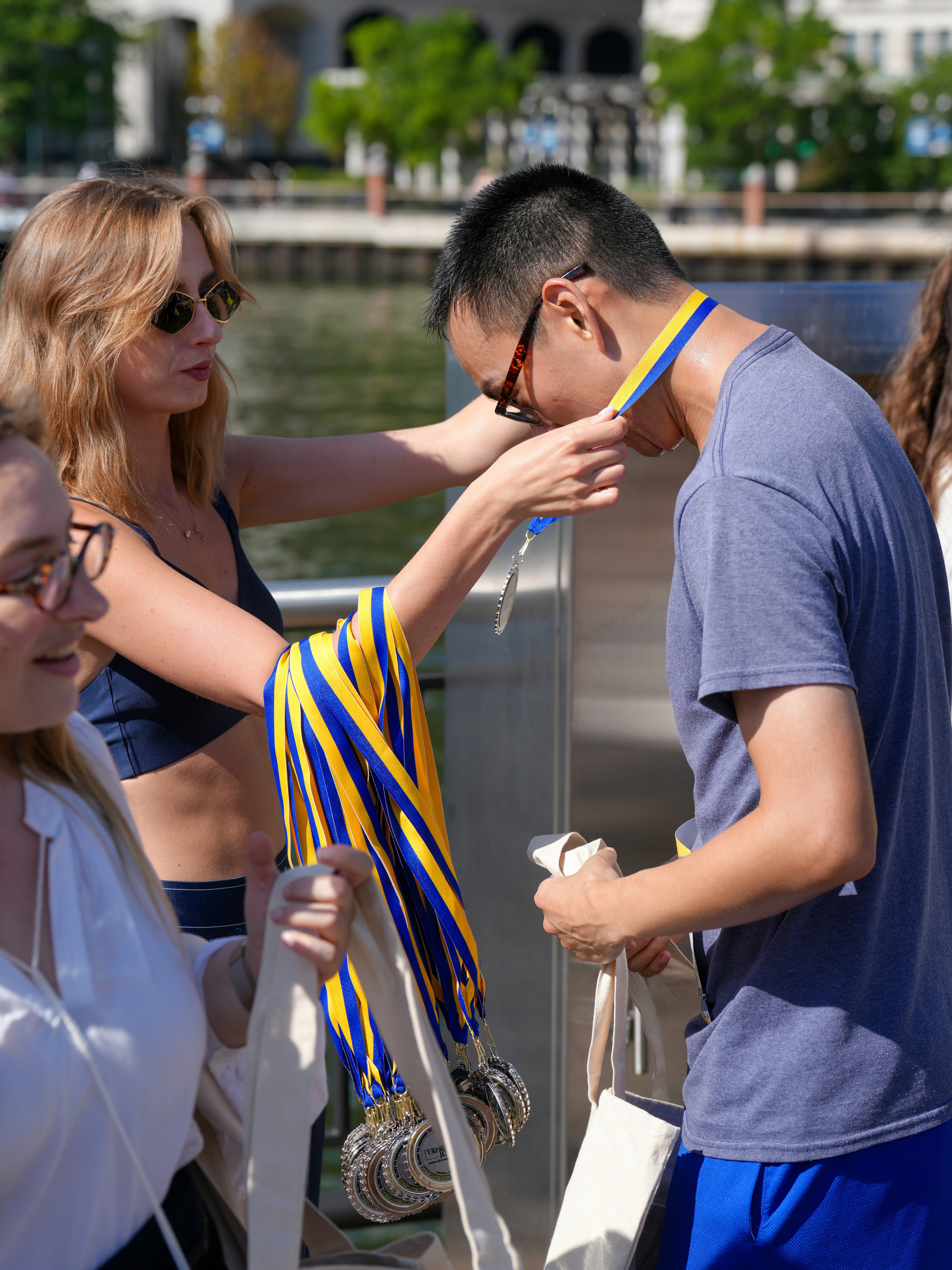 A woman placing a blue and yellow medal around a man's neck outdoors - race courses through history