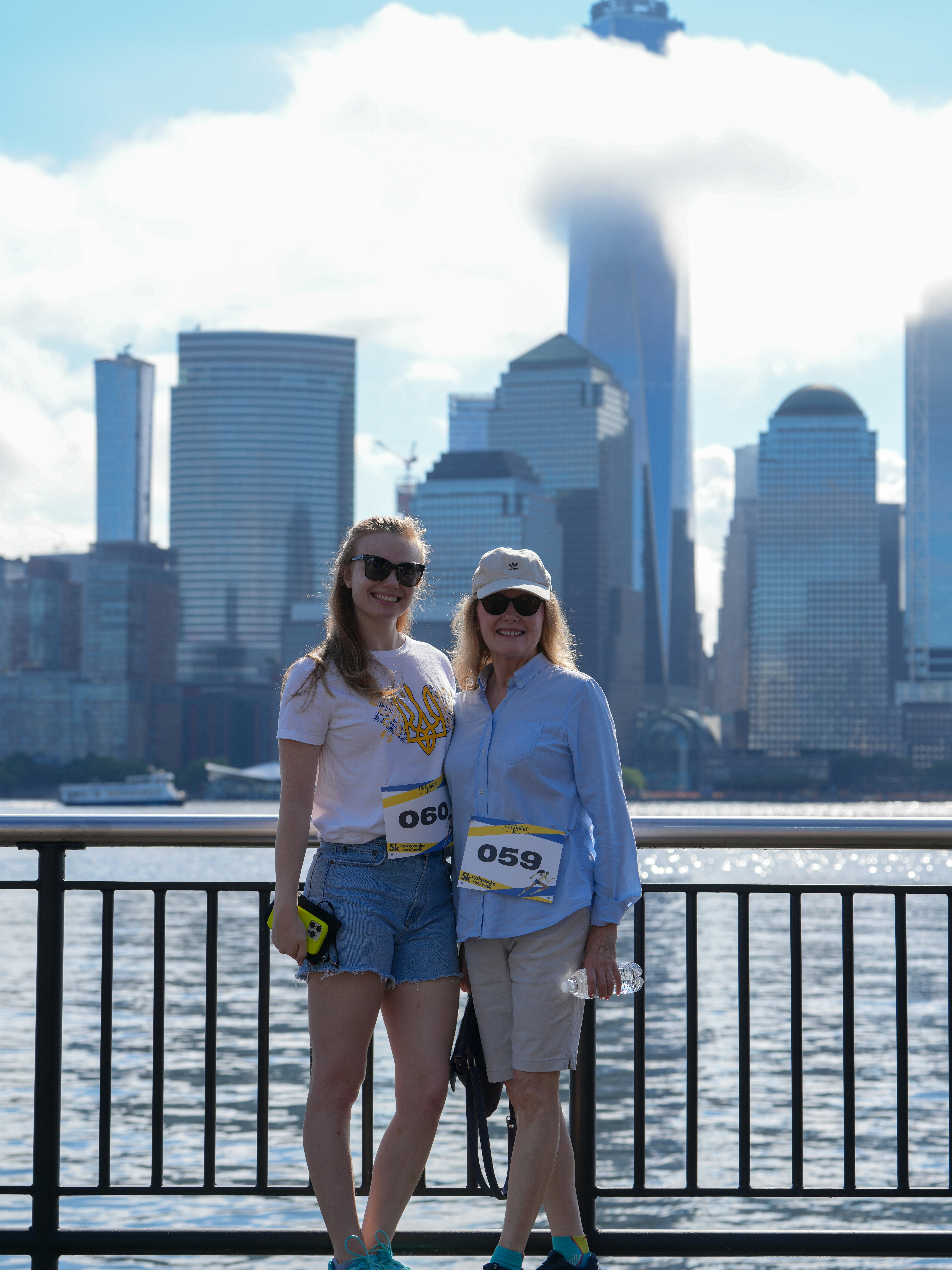 Two women wearing race bibs standing before the New York City skyline