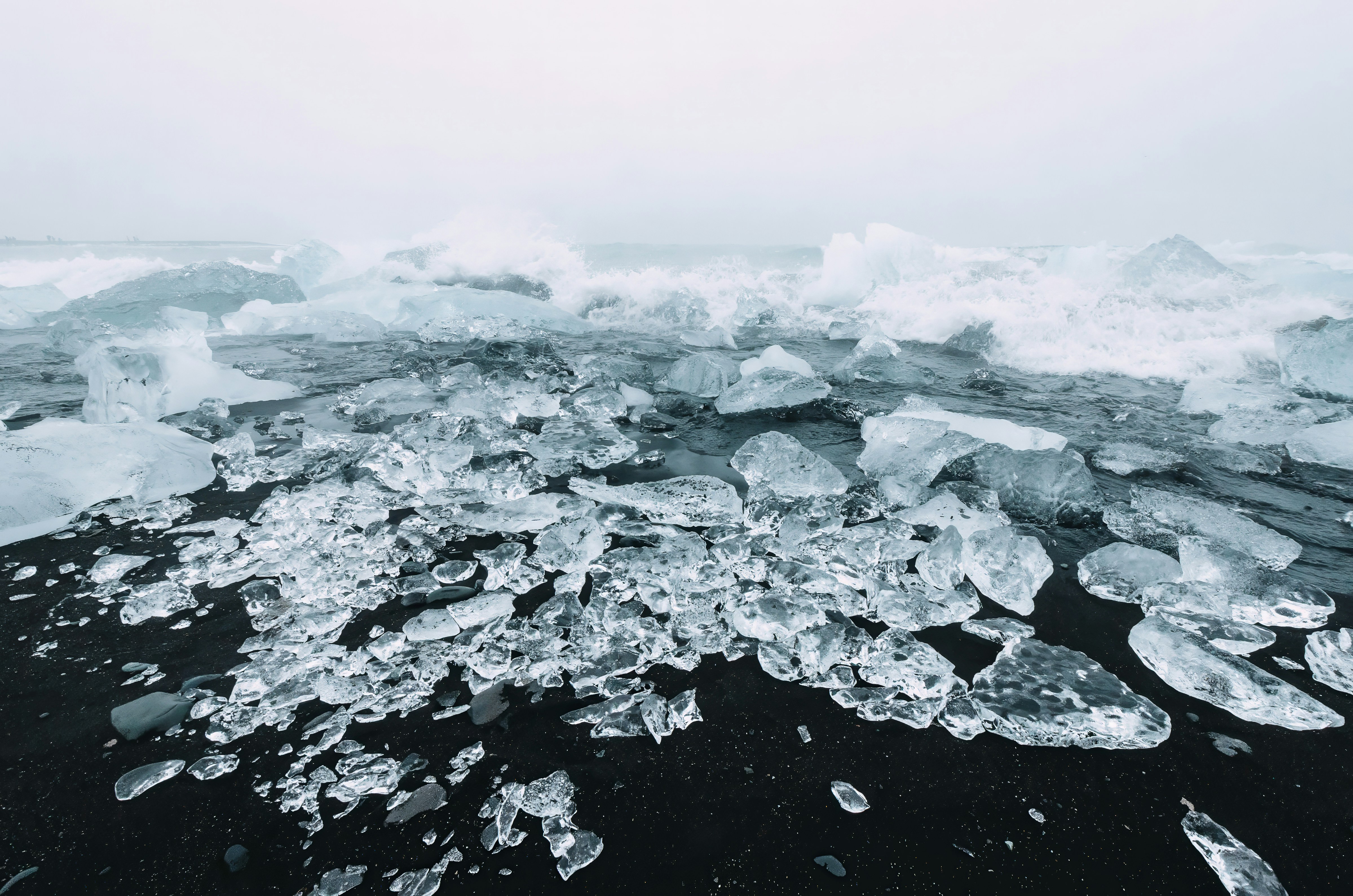 Chunks of clear ice on a black sand beach with crashing ocean waves