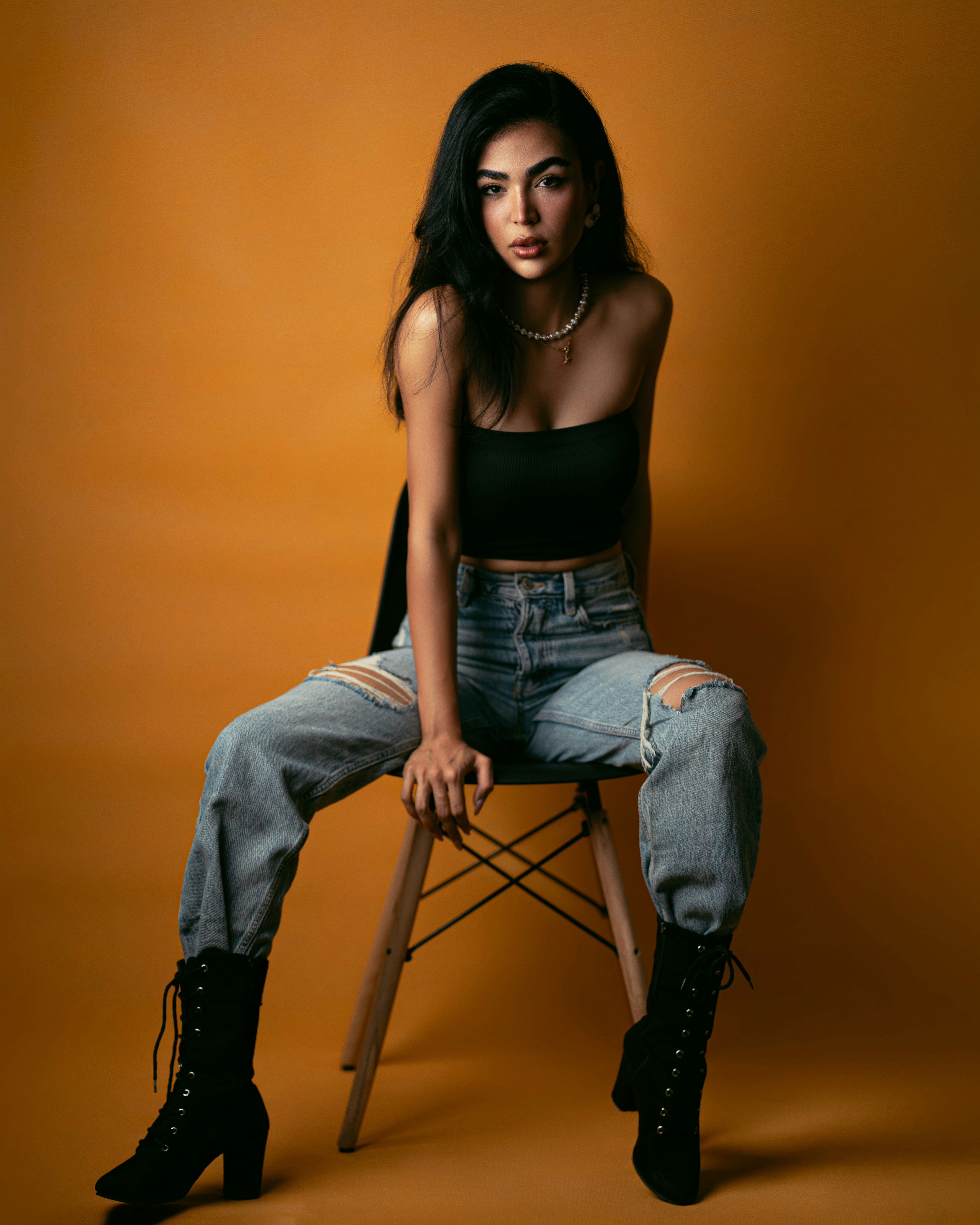 A woman in a black tube top and ripped jeans sitting on a chair