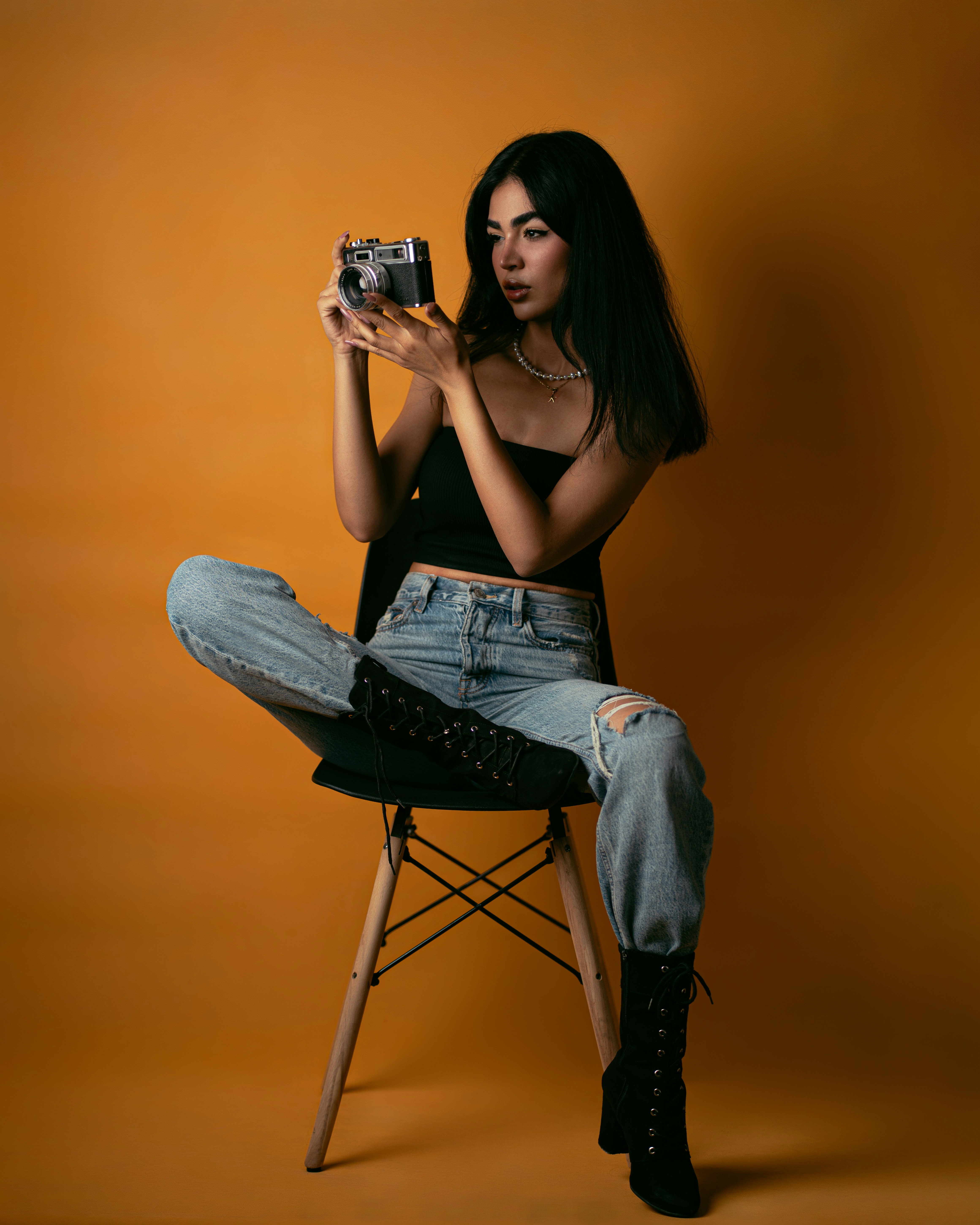 A woman in a black top and jeans holding a vintage camera on a chair