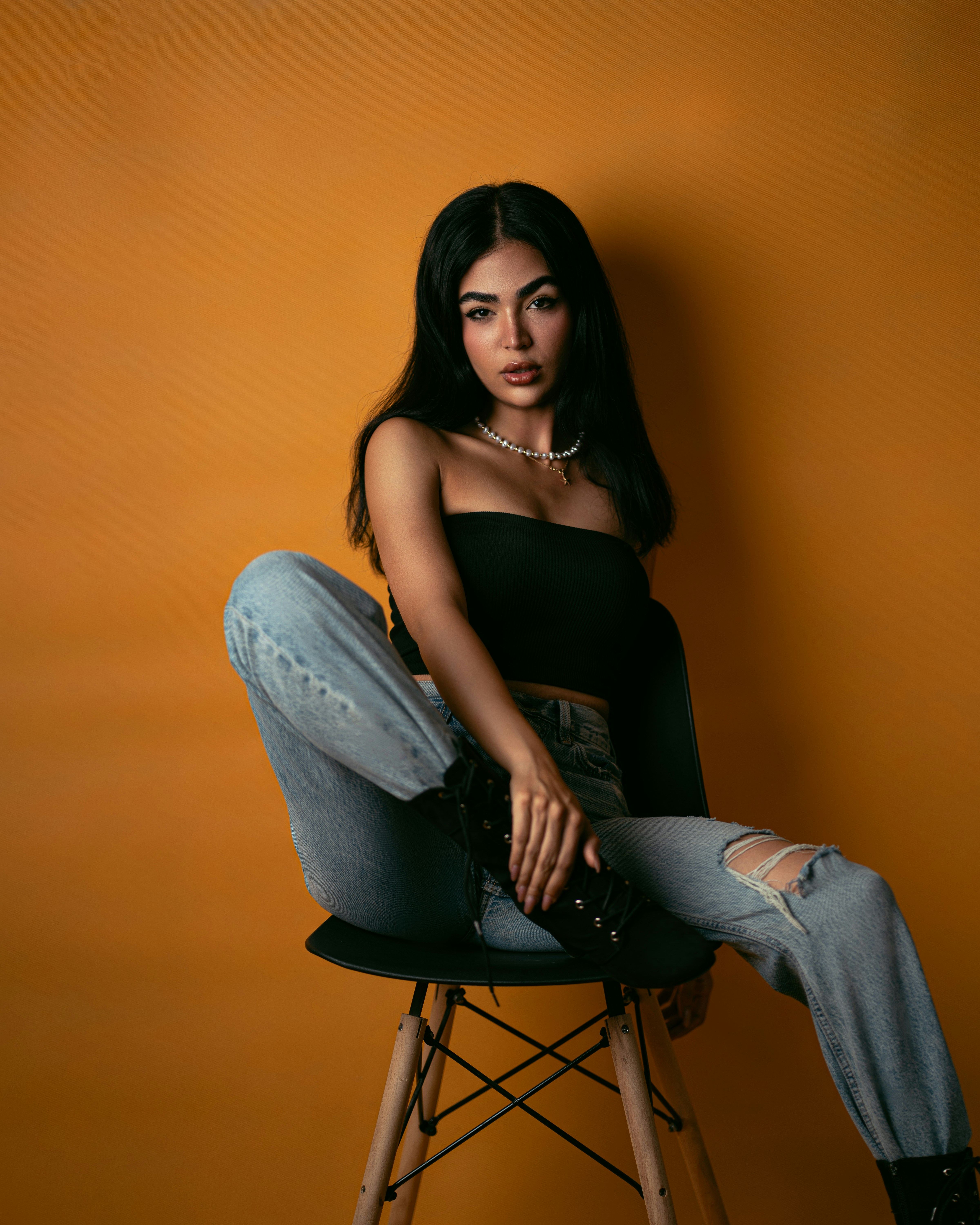A woman in a black tube top and ripped jeans sitting on a chair