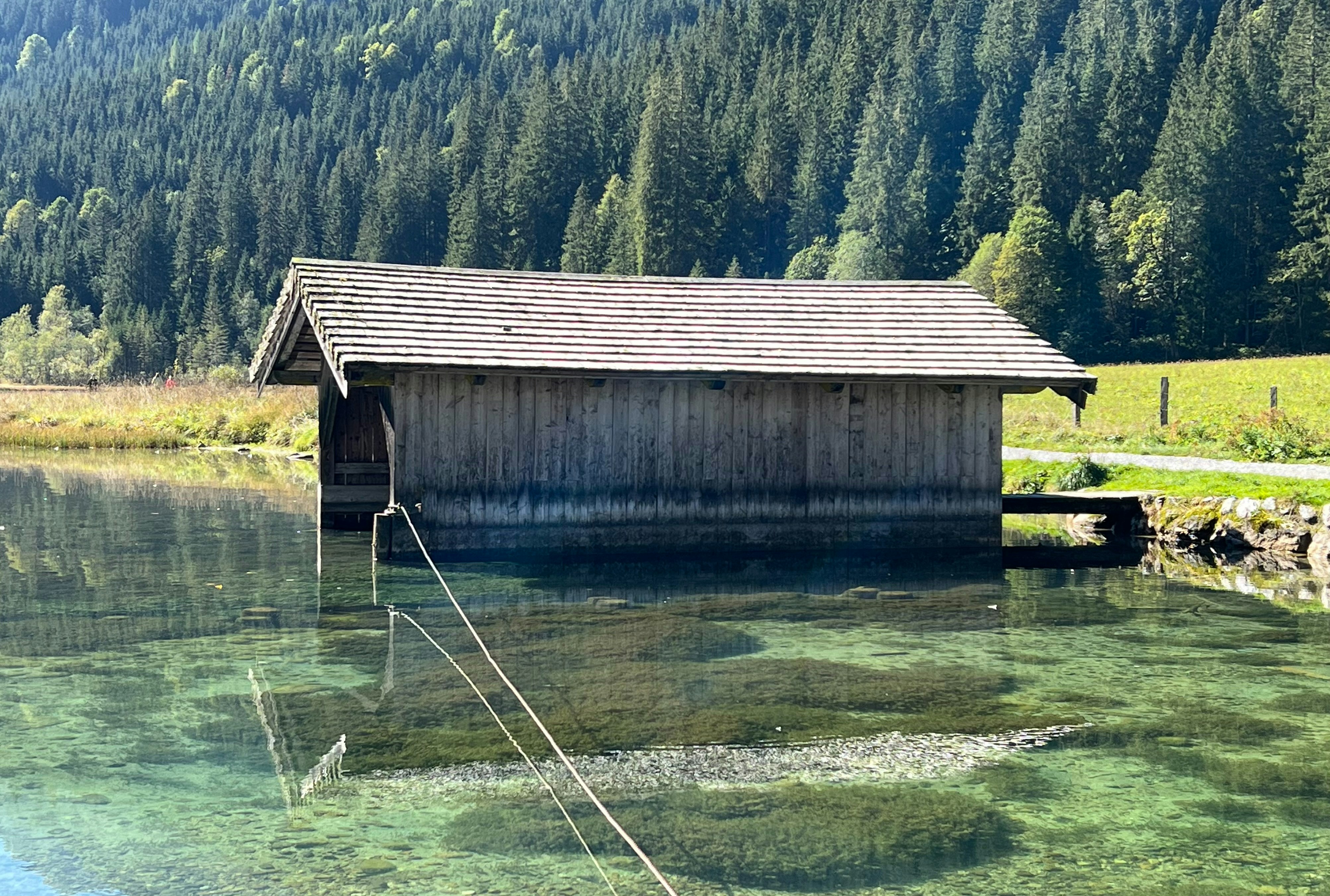 A wooden boathouse on a clear lake with a dense pine forest background
