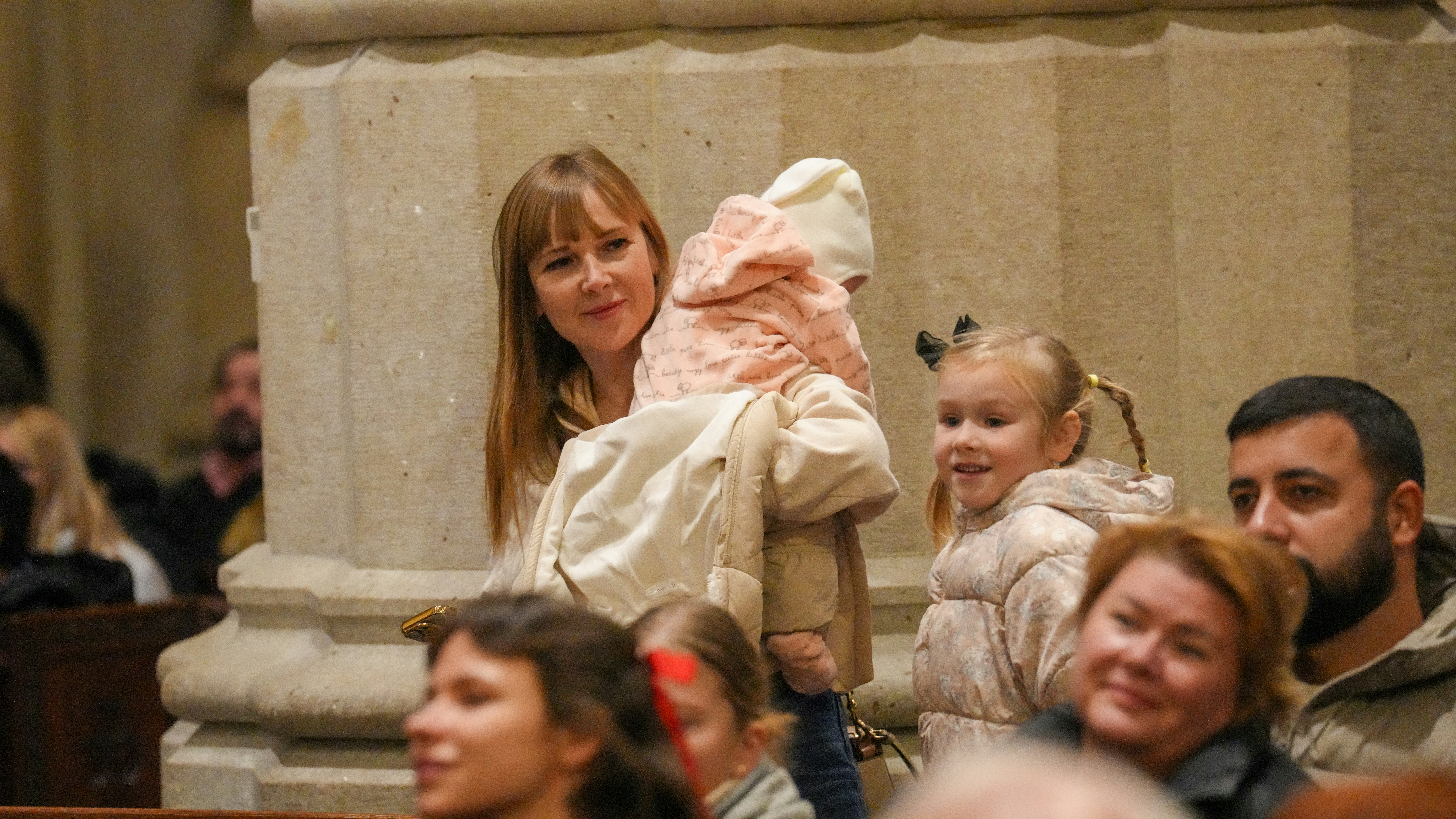 A woman holding a baby in a light jacket beside a young girl