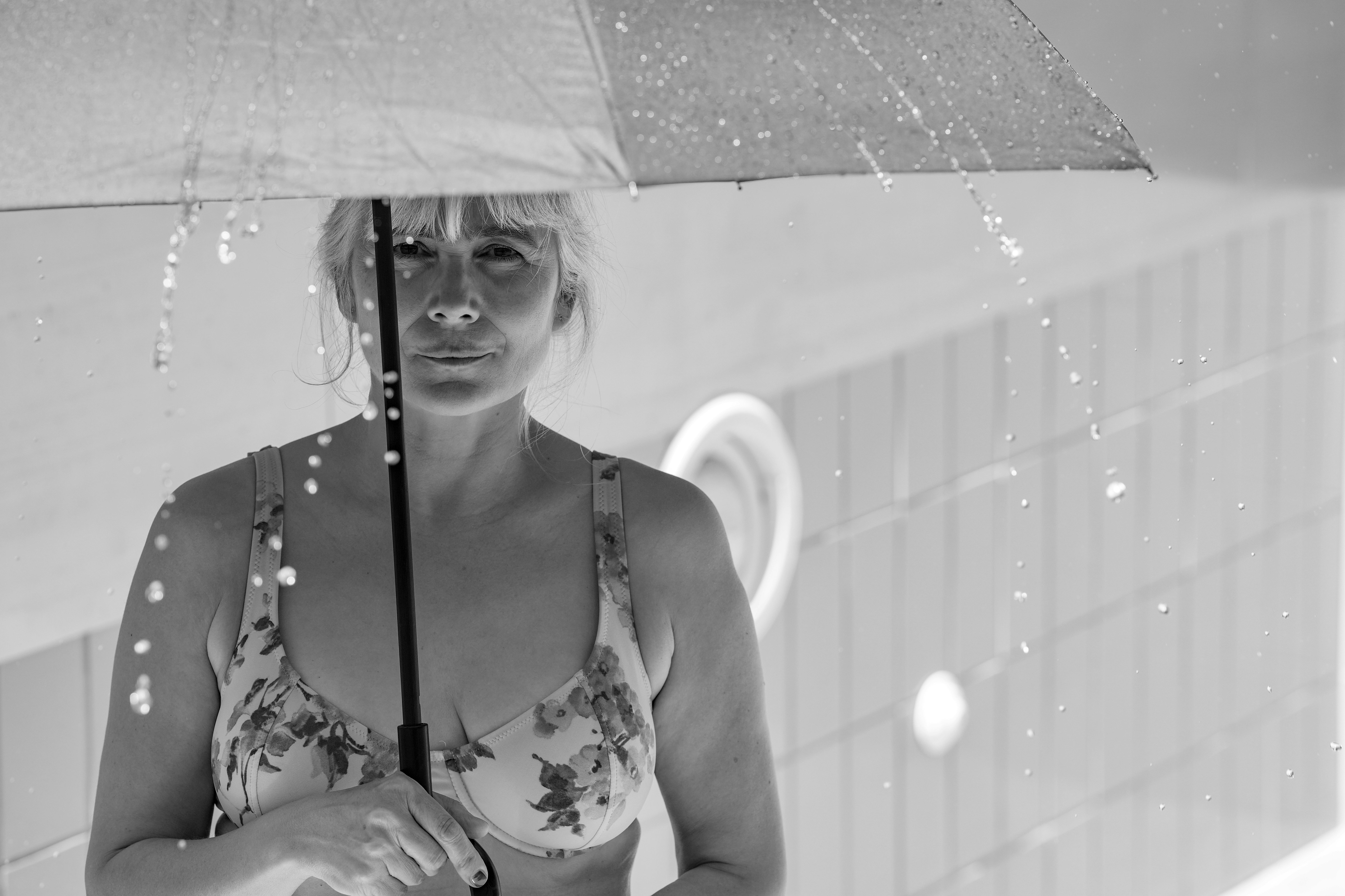 Una donna in bikini floreali che tiene un ombrello sotto la pioggia