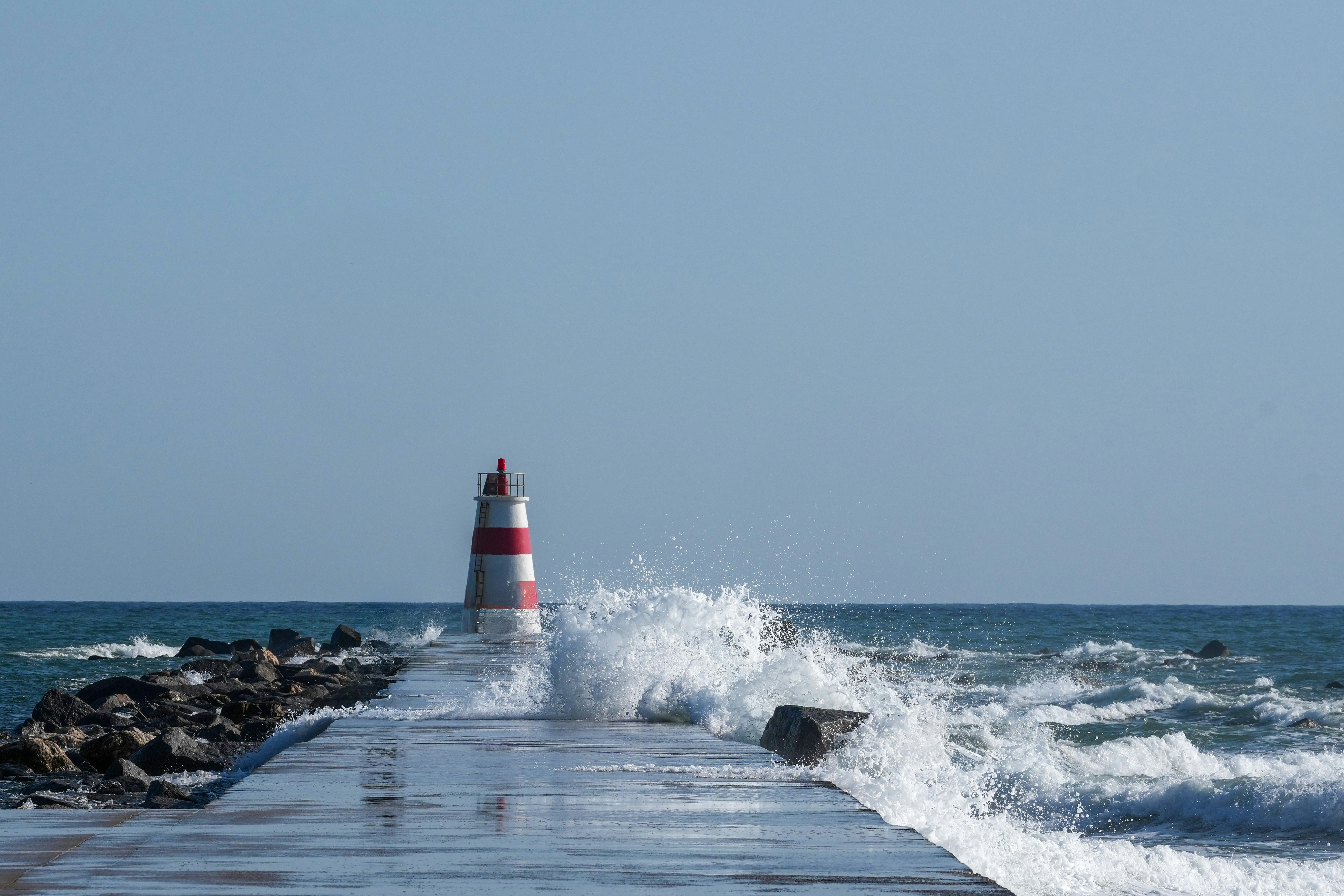 Un faro rosso e bianco su un molo di cemento con onde oceaniche che si infrangono