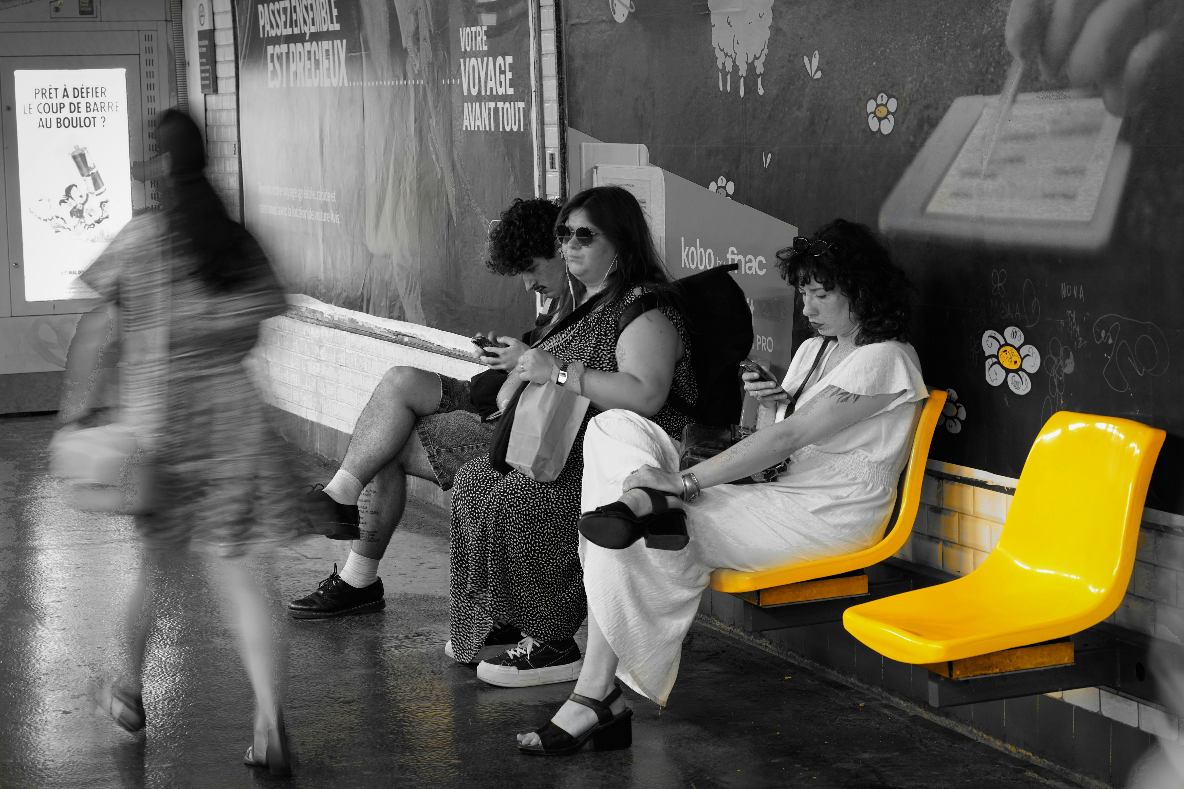 Due persone sedute sui sedili gialli della metropolitana mentre una persona passa