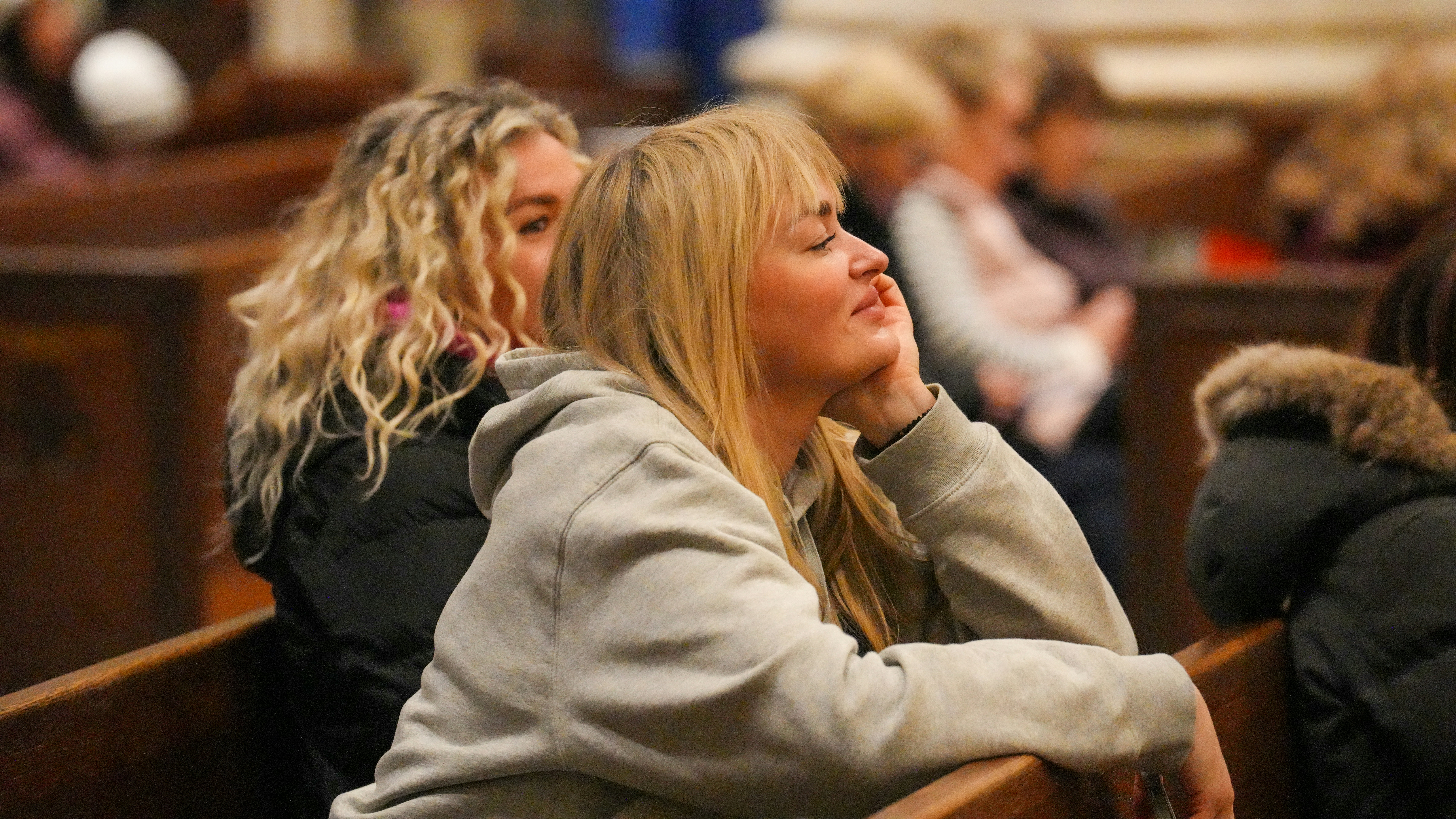 A woman with blonde hair resting her chin on her hand in a church