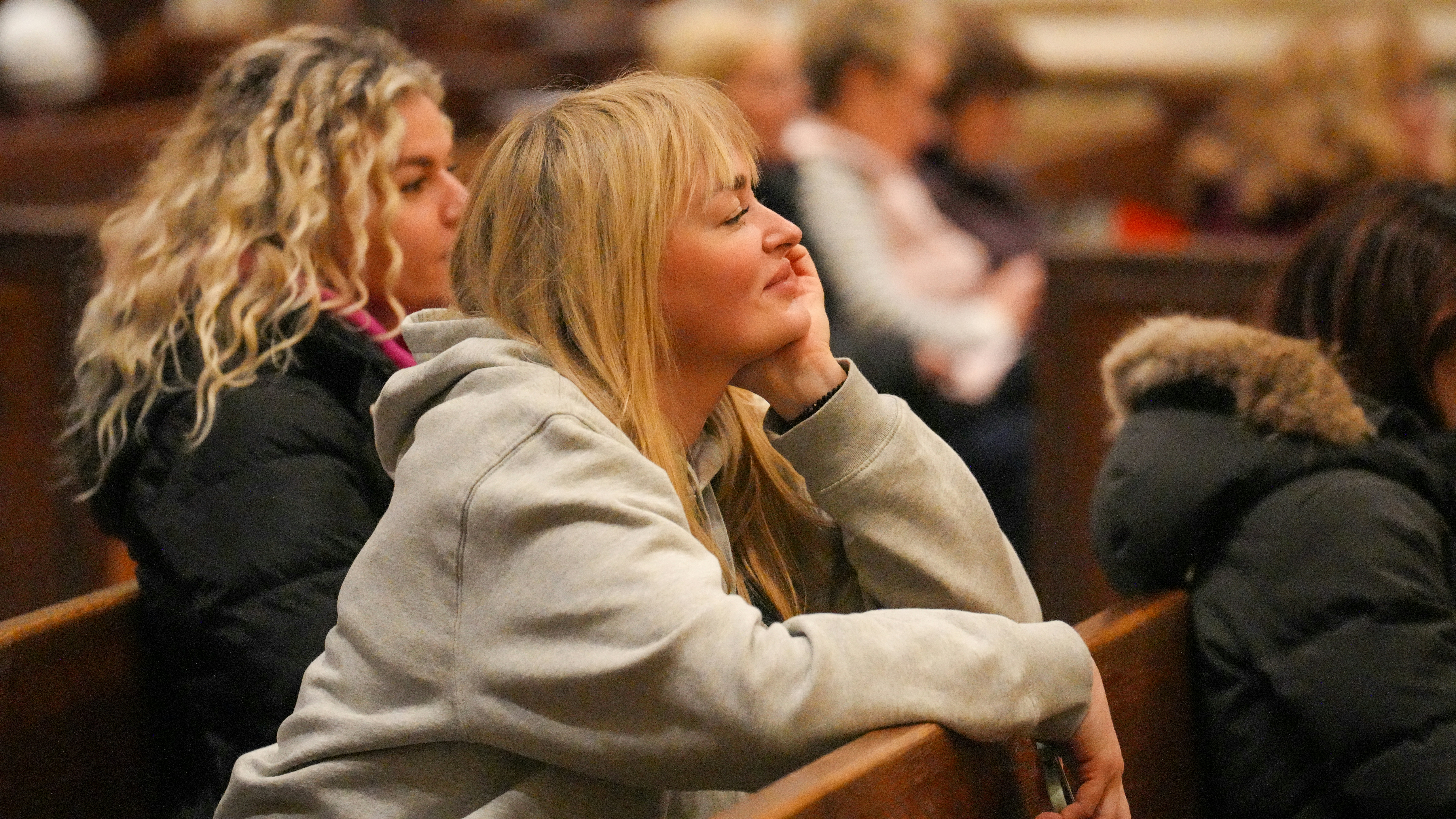 A woman with blonde hair resting her chin on her hand in a church