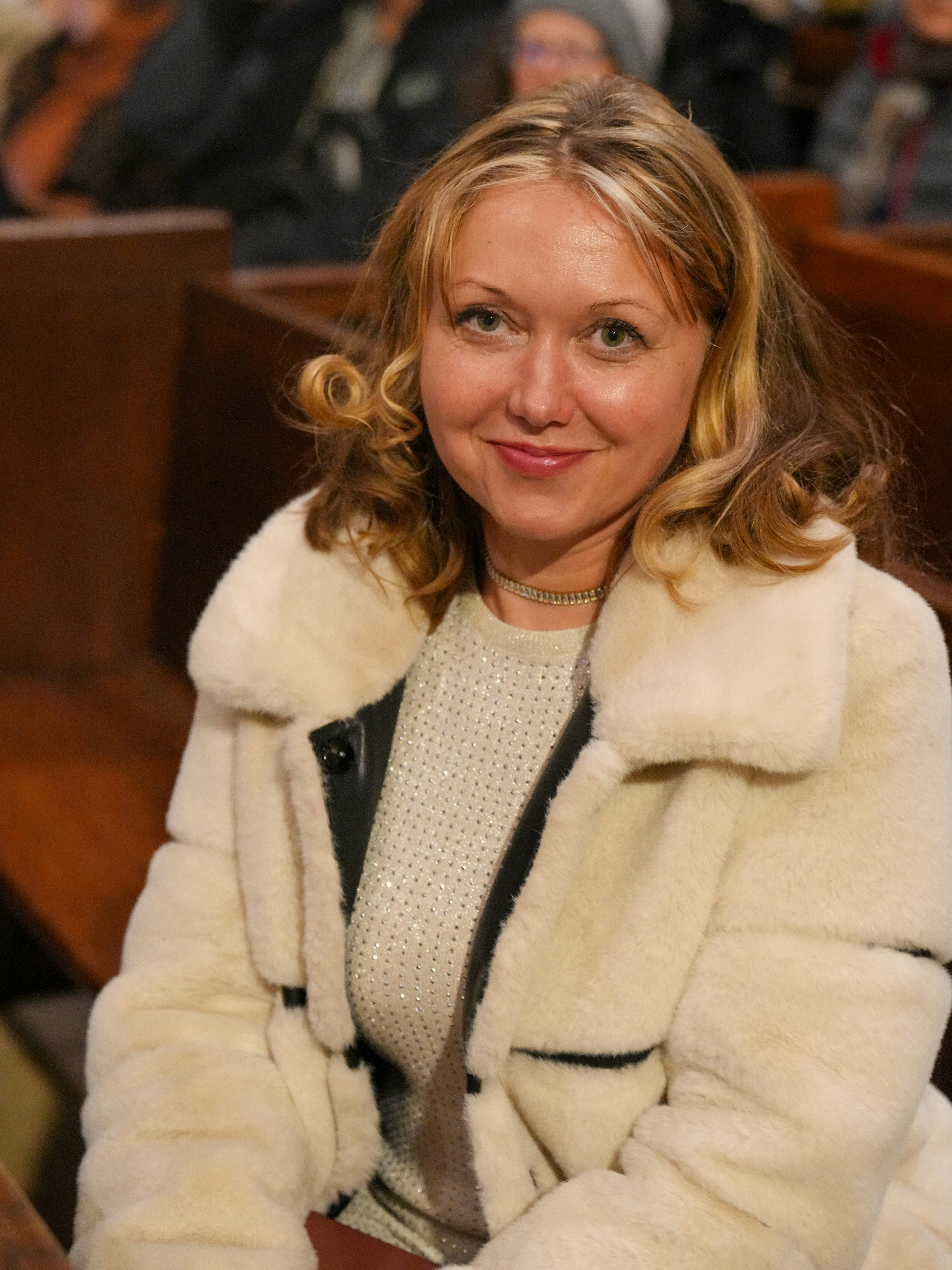 A woman with blonde hair wearing a cream faux fur coat in a church