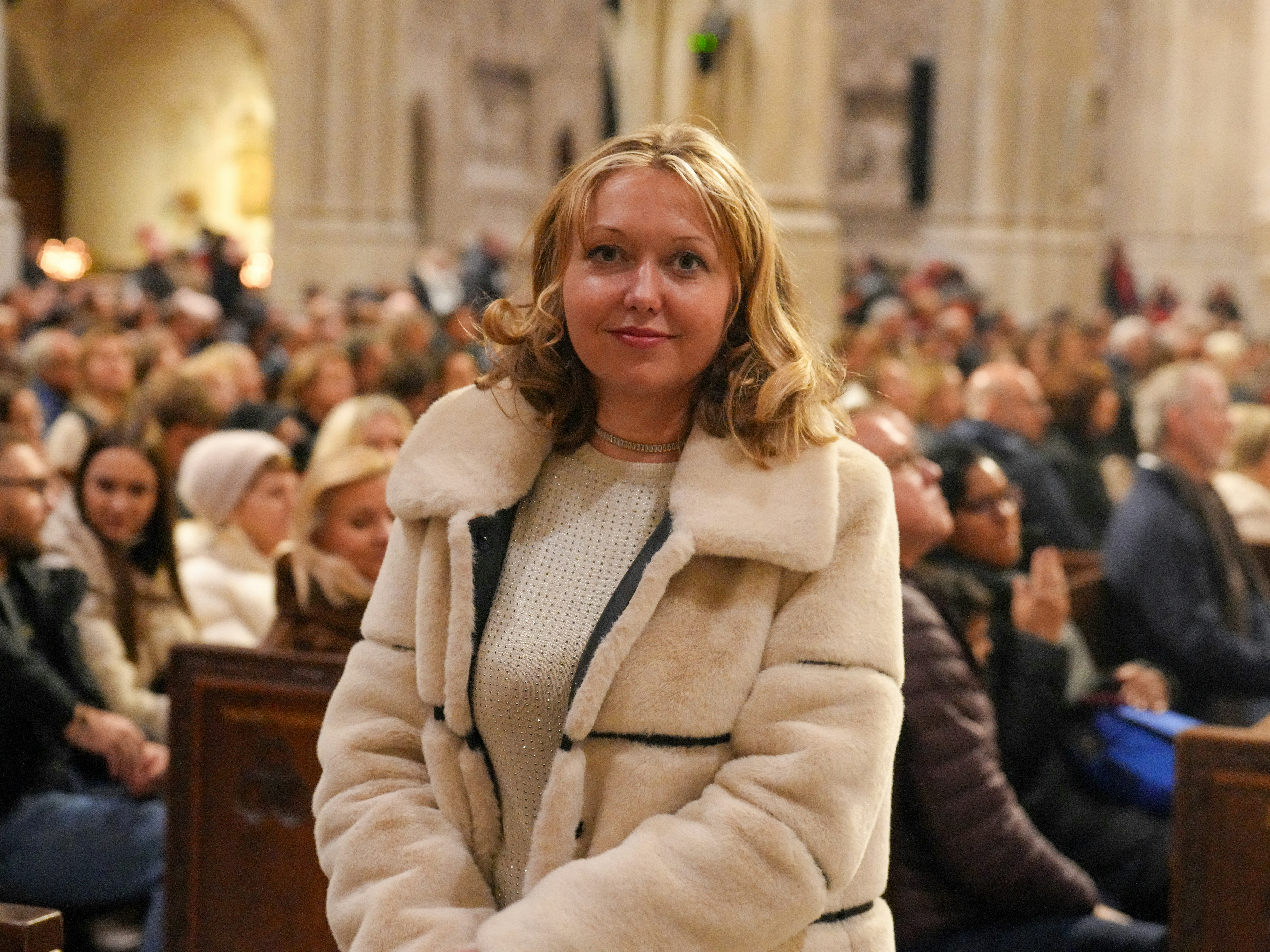 A woman in a cream faux fur coat sitting in a crowded church