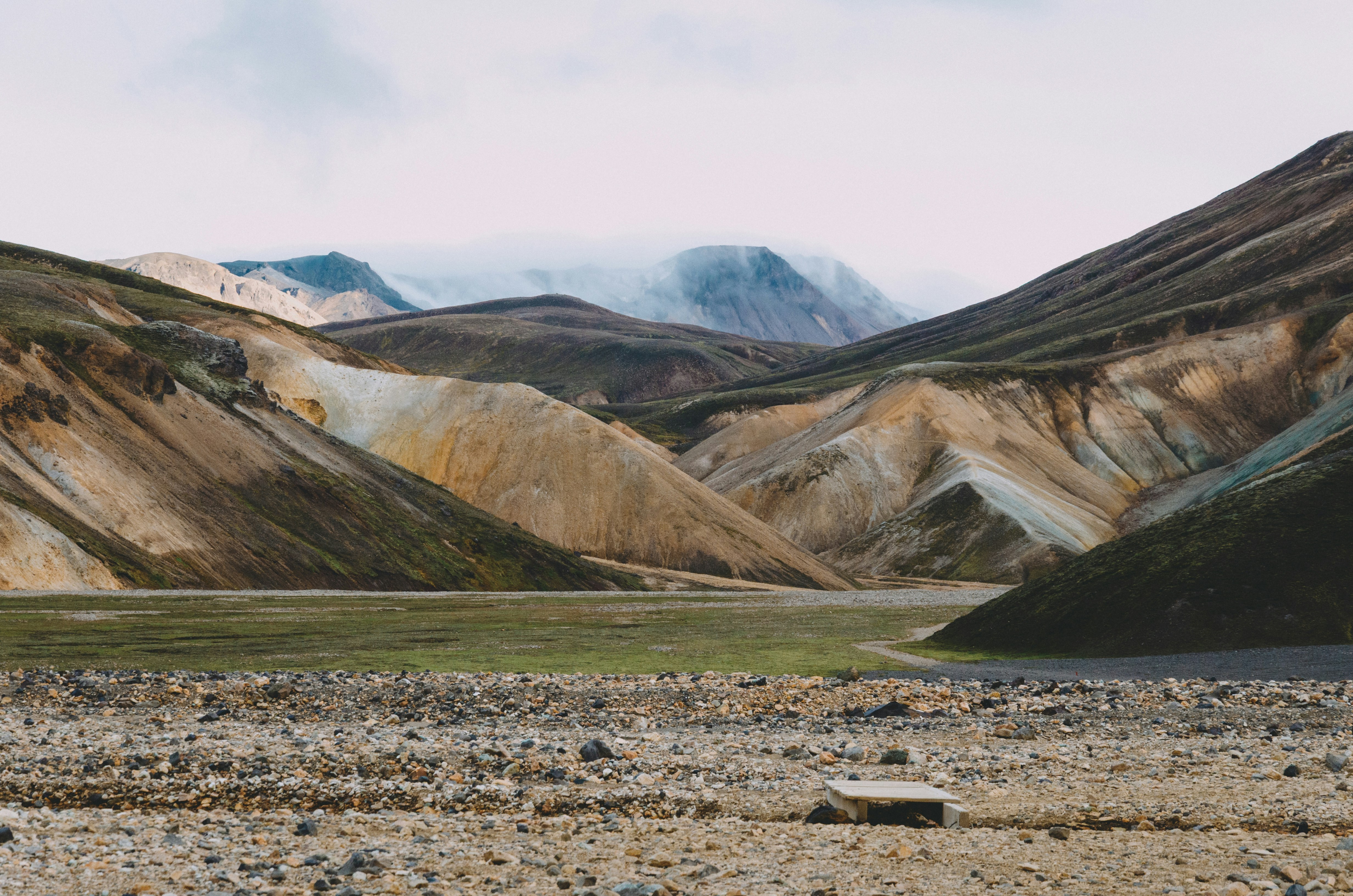 A rocky valley floor leading to colorful rhyolite mountains under a cloudy sky