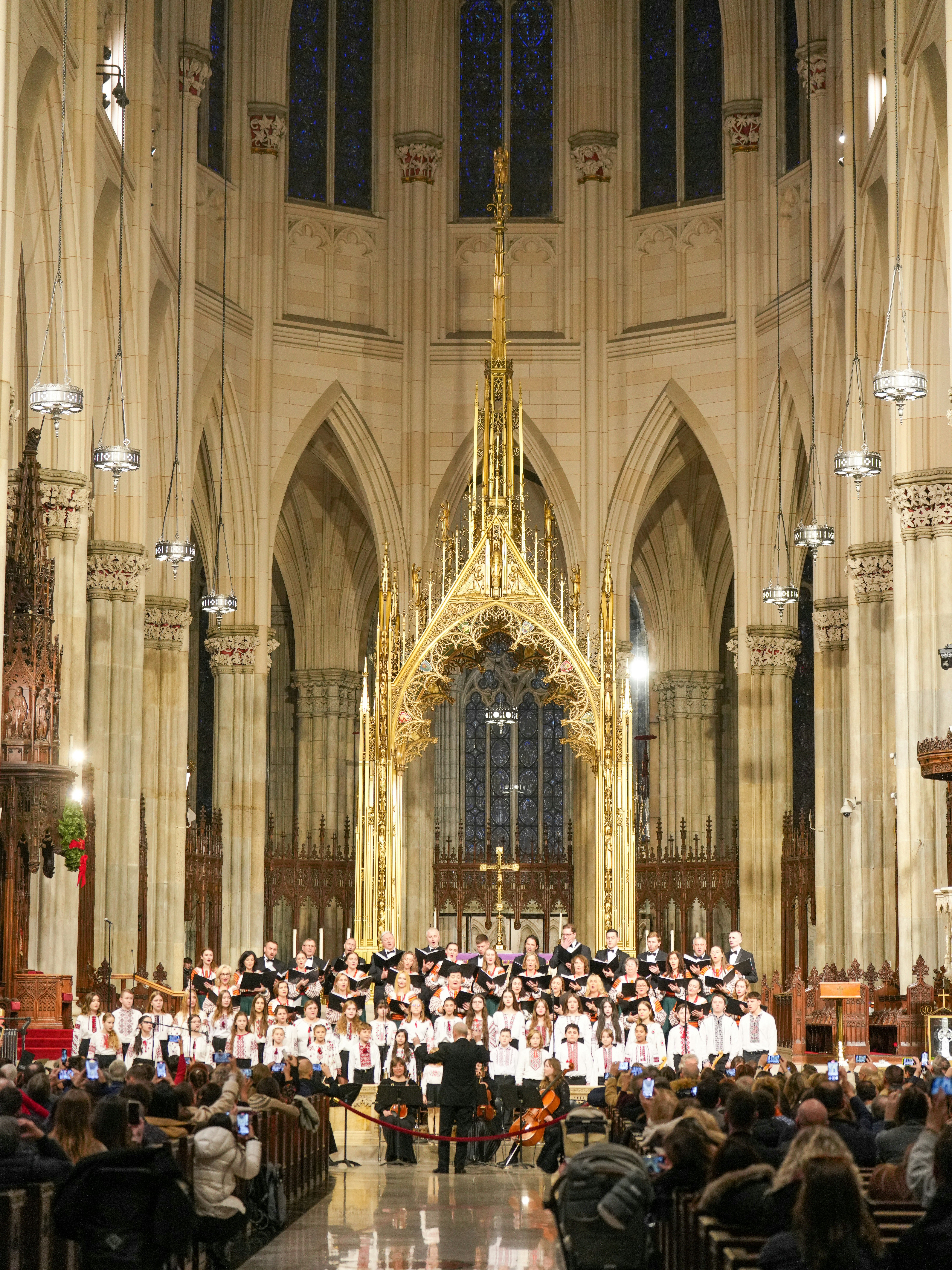 A large choir in white shirts performing in a gothic cathedral with gold altar