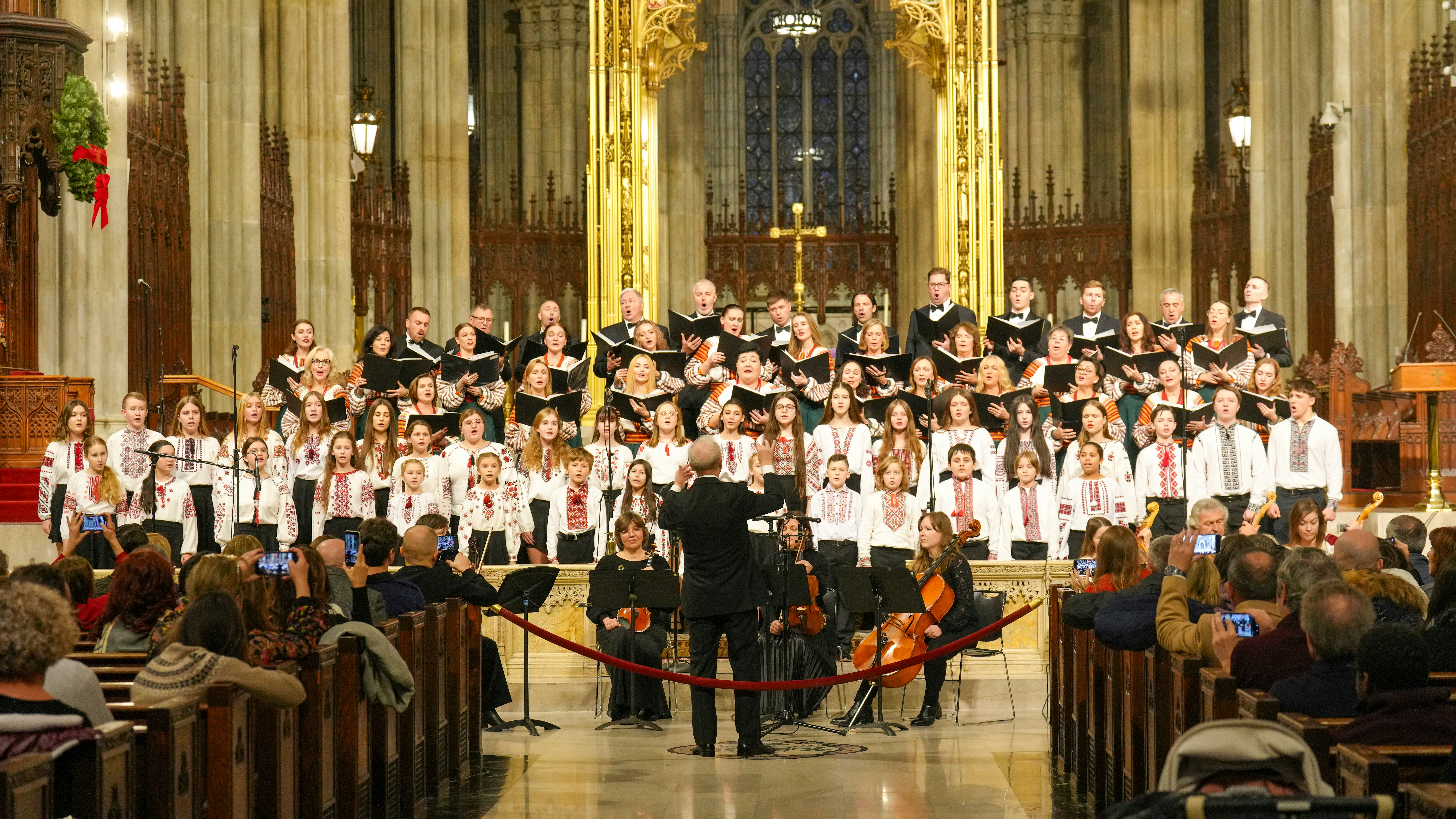 A large choir in traditional embroidered shirts singing in a cathedral with a conductor