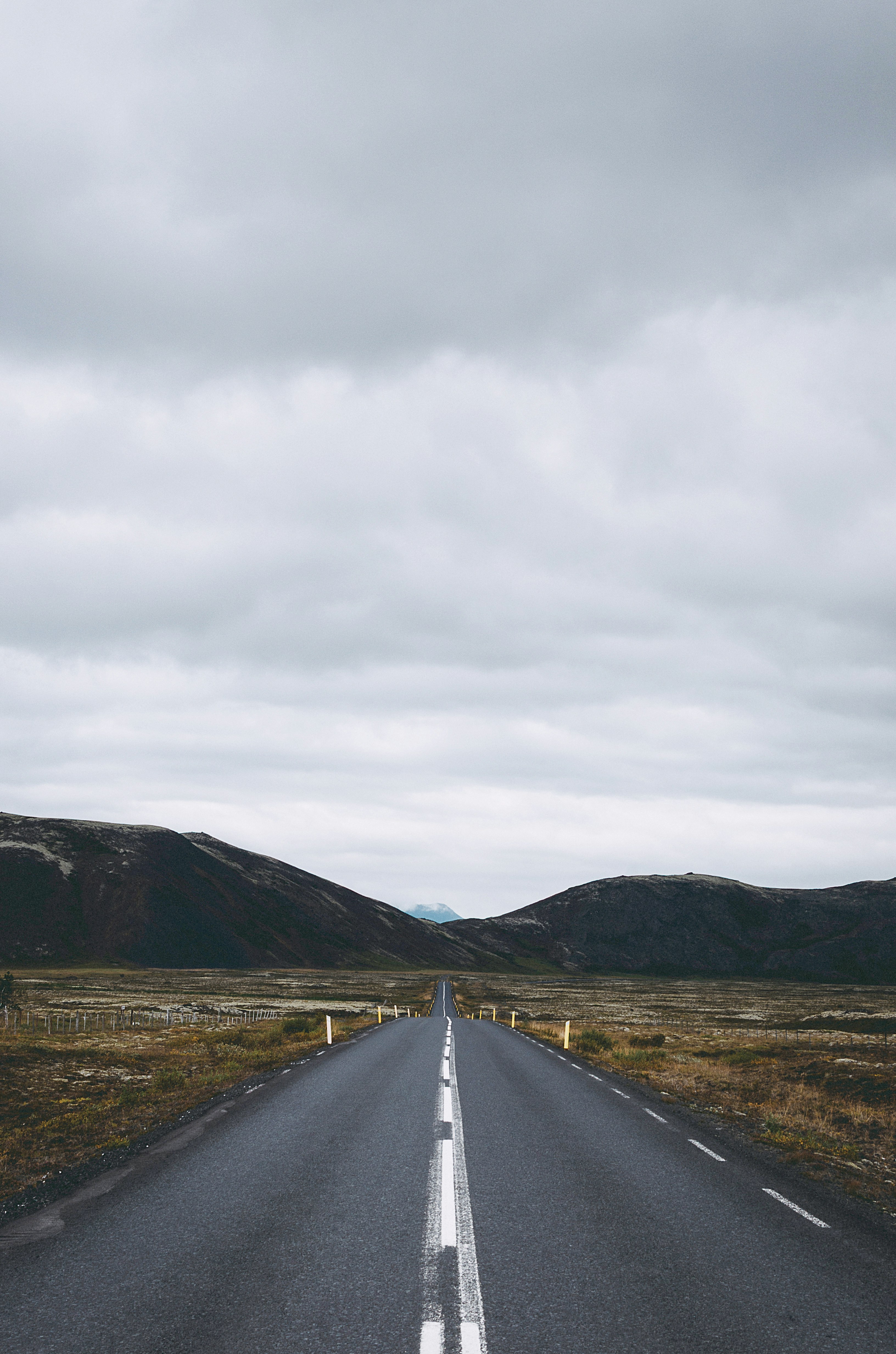 An asphalt road stretching through a vast landscape of rolling hills under cloudy skies