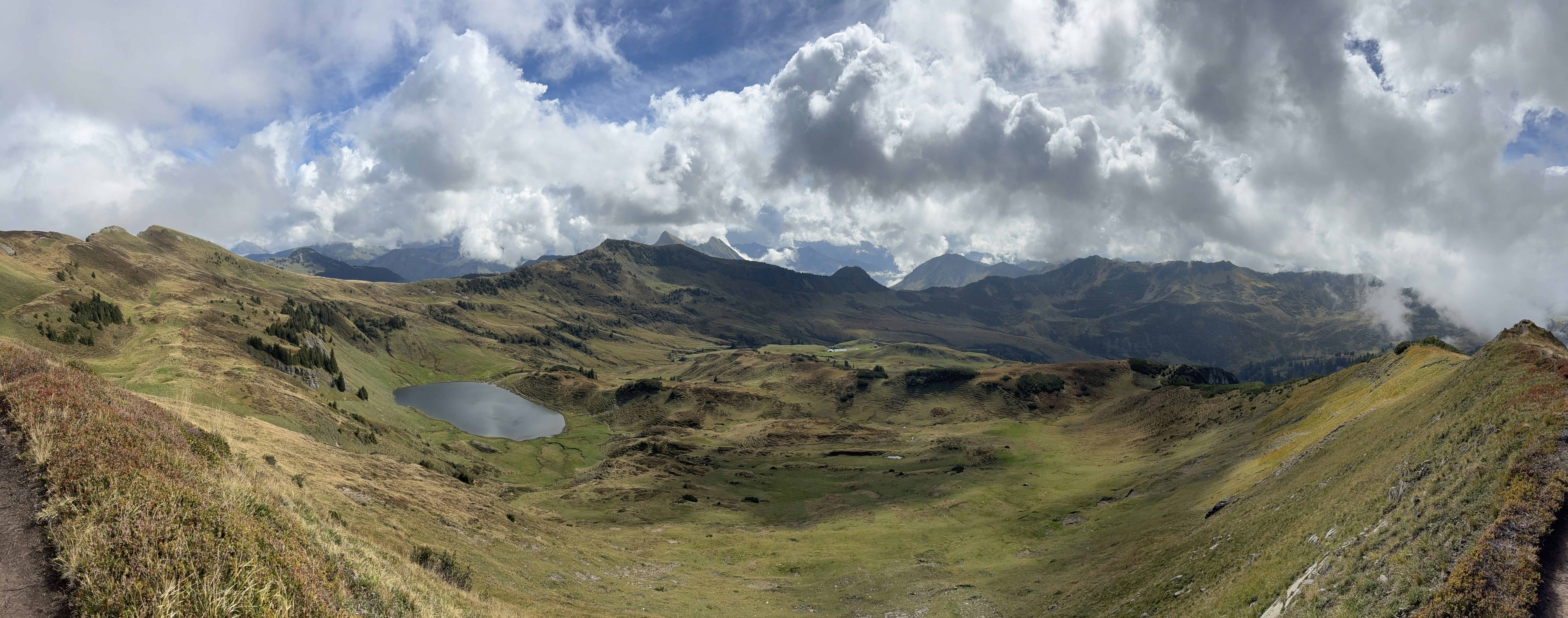 A panoramic view of a mountain lake in a grassy alpine valley