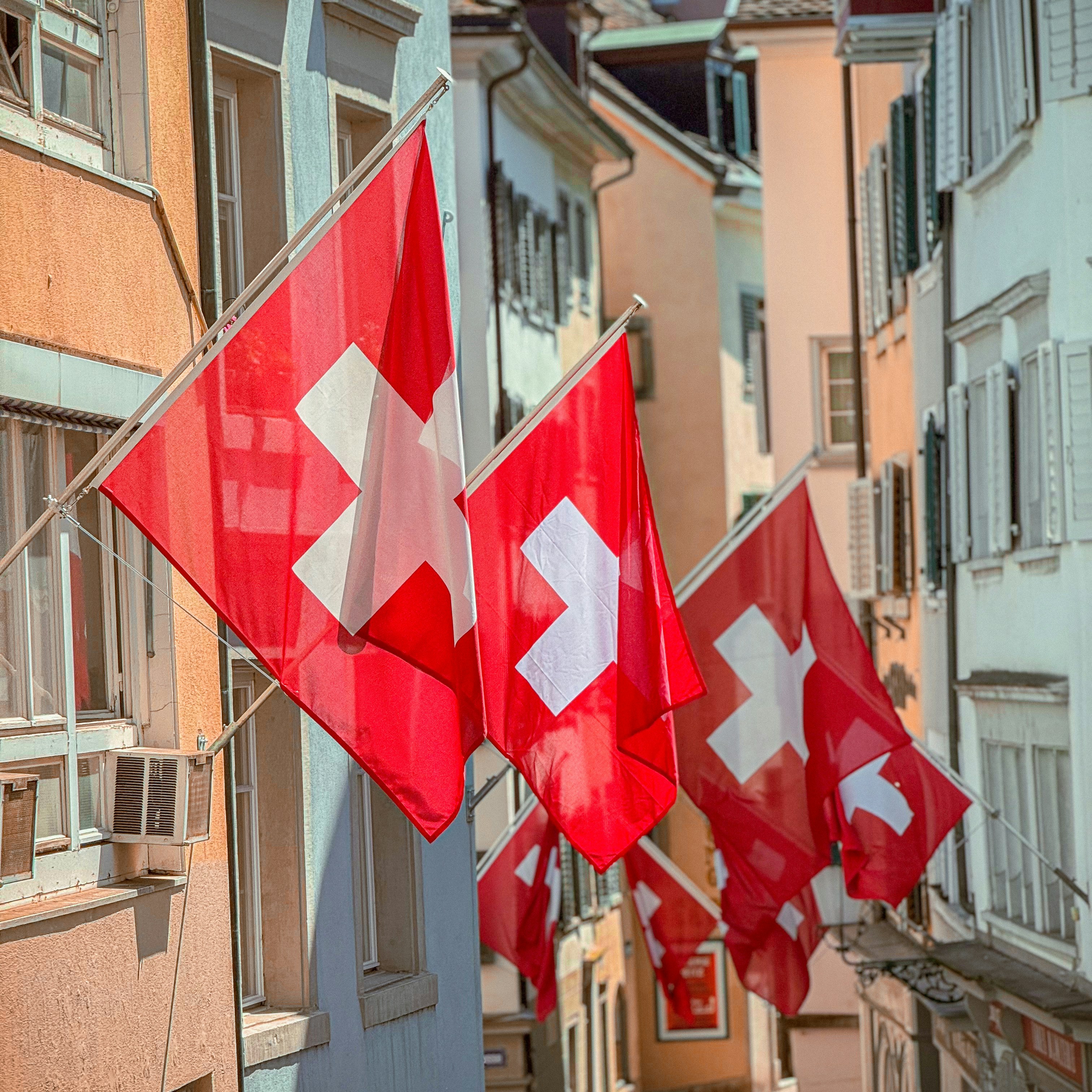 Swiss flags hanging from buildings along a narrow street in Switzerland