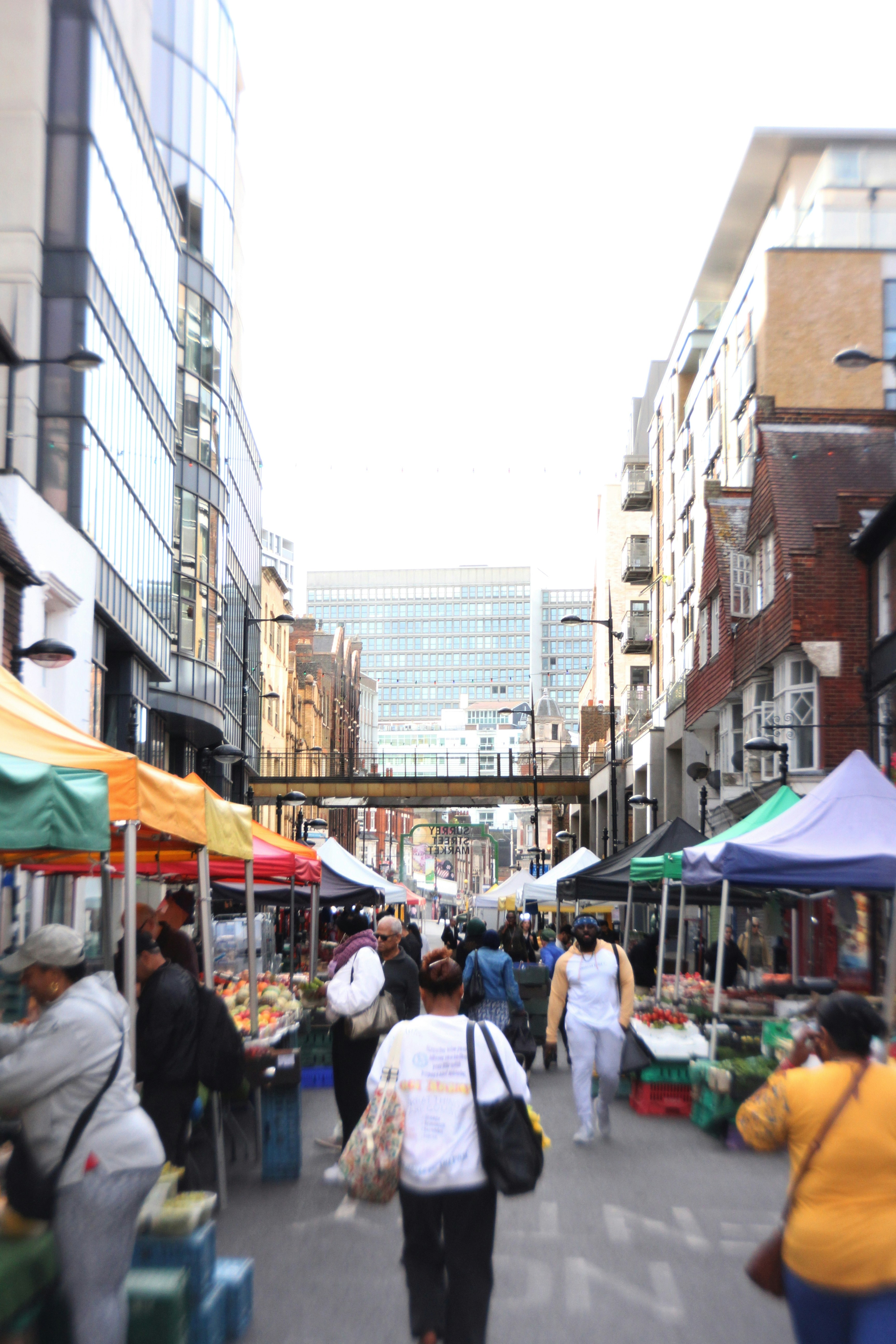 People walking through a busy outdoor market with colorful stalls in London