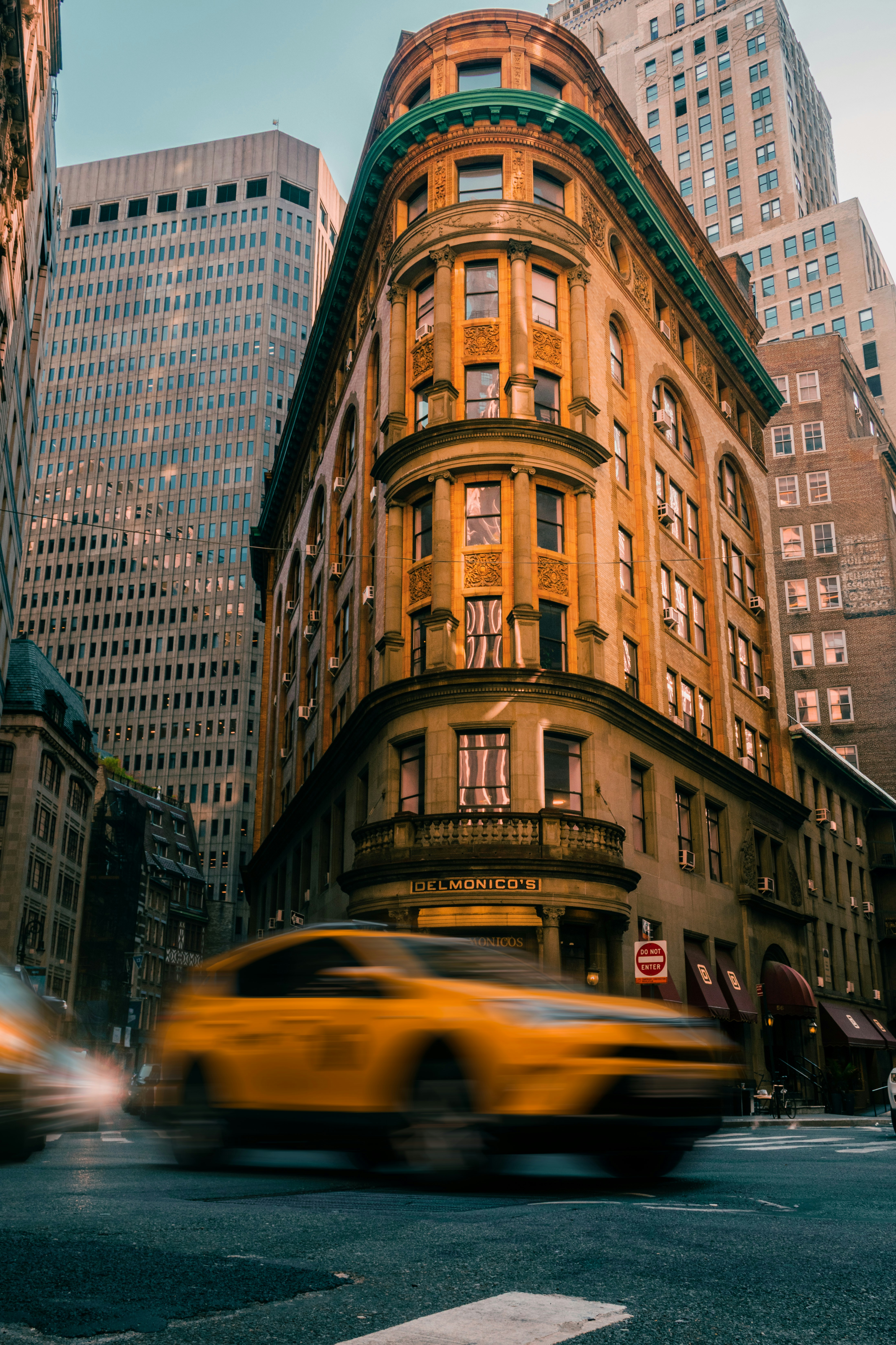 A yellow taxi driving past the historic Delmonico's building in New York City