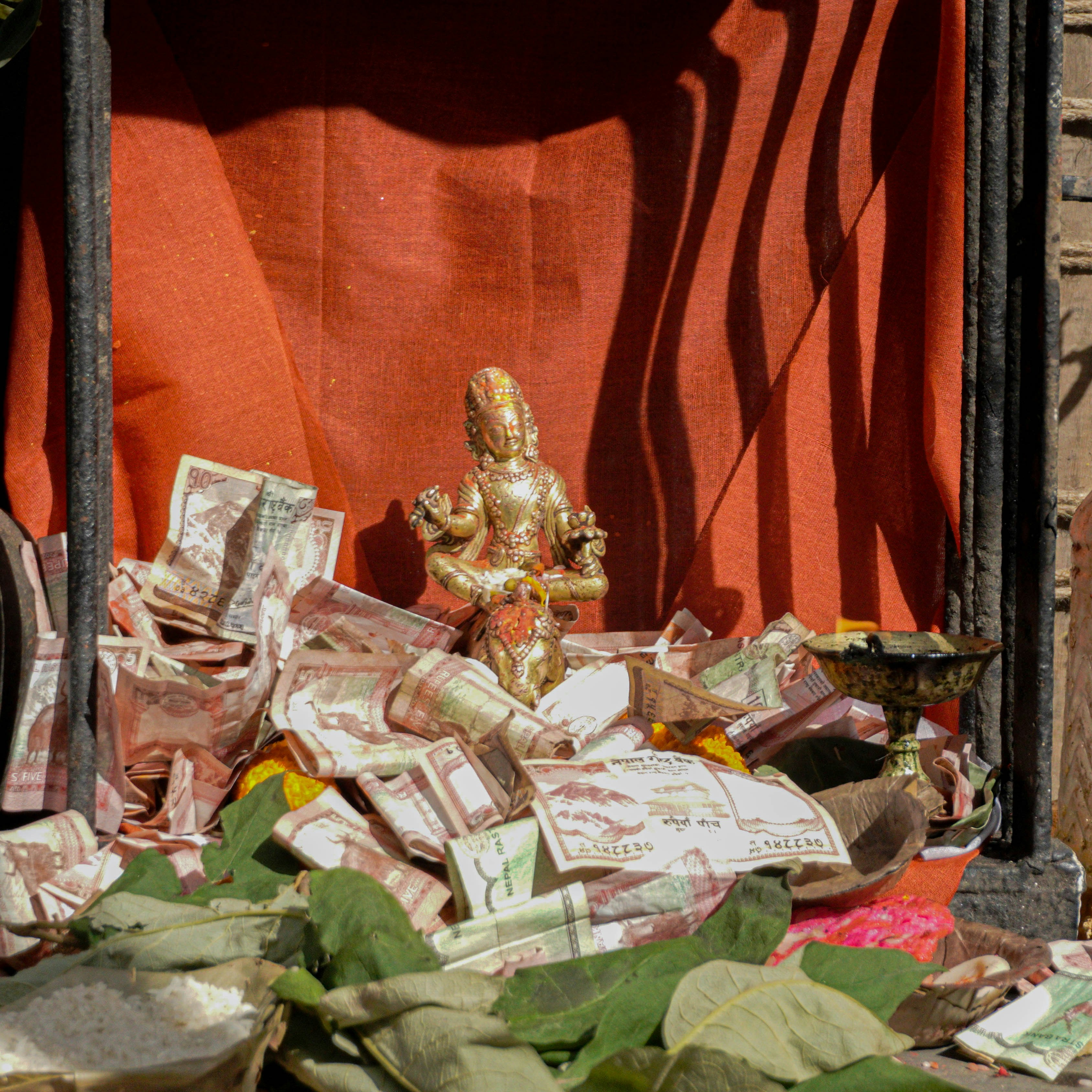 A small golden deity statue surrounded by paper currency and green leaves