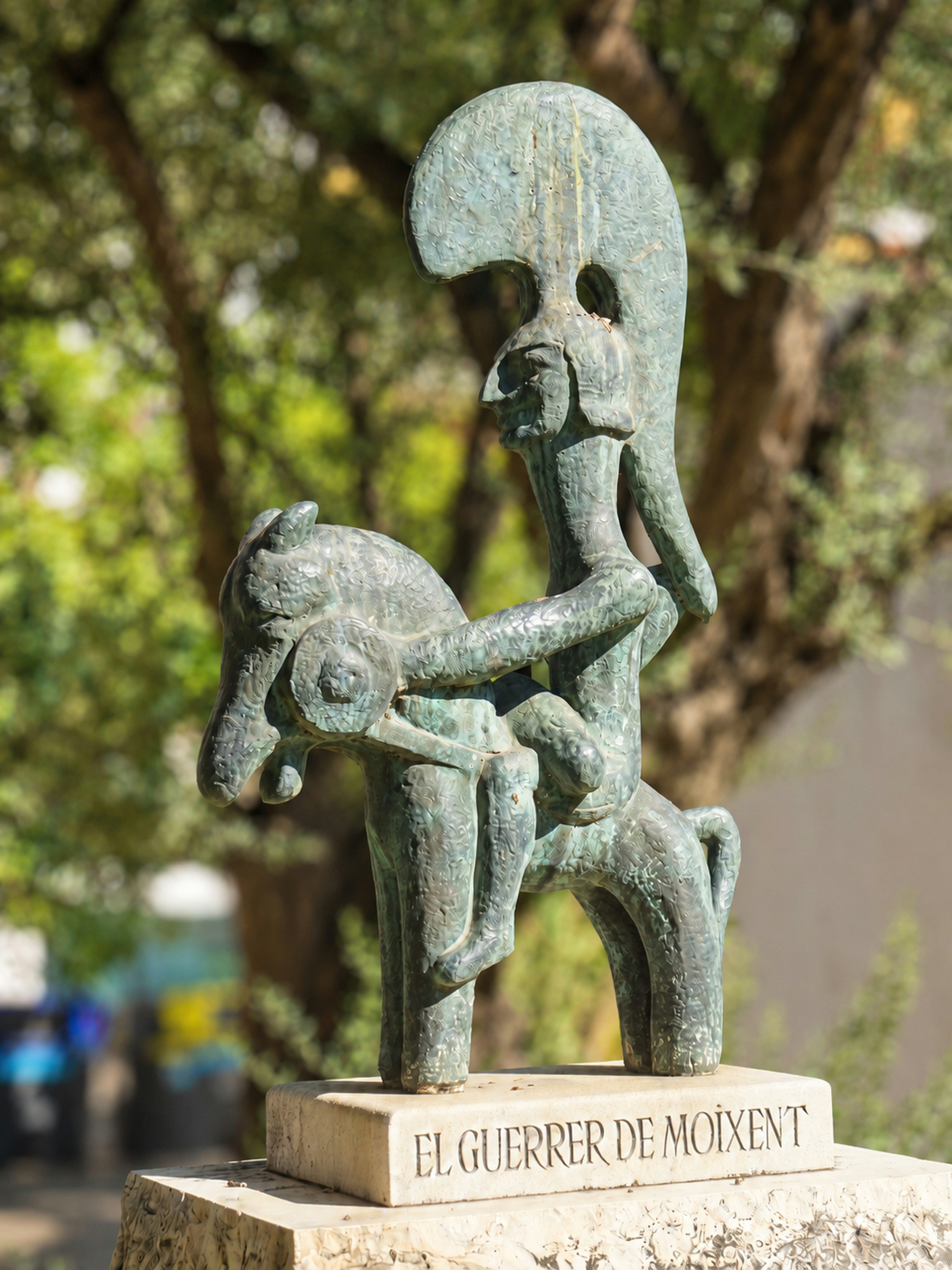Una estatua de bronce de un guerrero a caballo con un alto casco en un parque