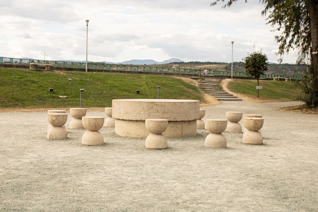 A circular stone table surrounded by hourglass shaped stone stools in a park