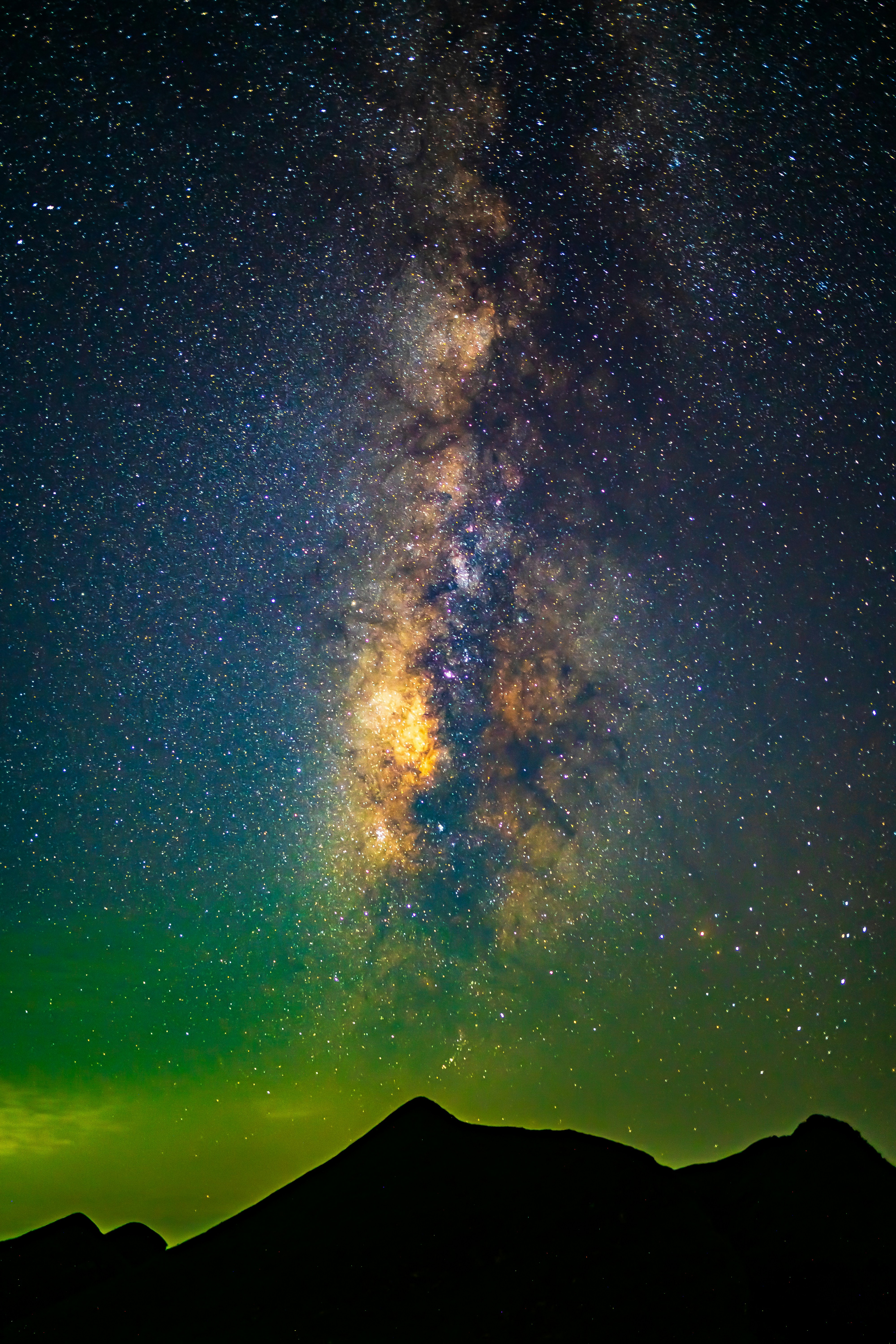 The Milky Way galaxy glowing above a dark mountain silhouette at night